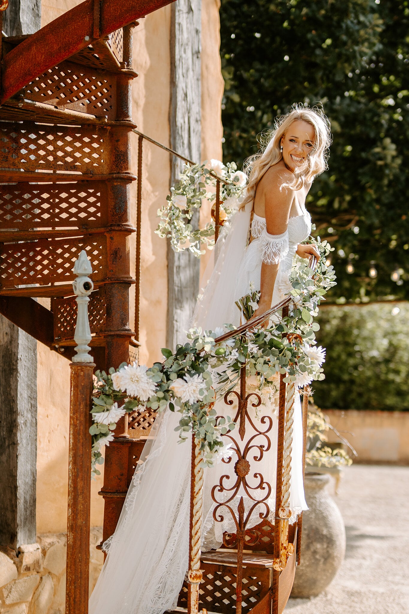Samantha smiles over her shoulder on the rust-red spiral staircase wrapped in flowers.