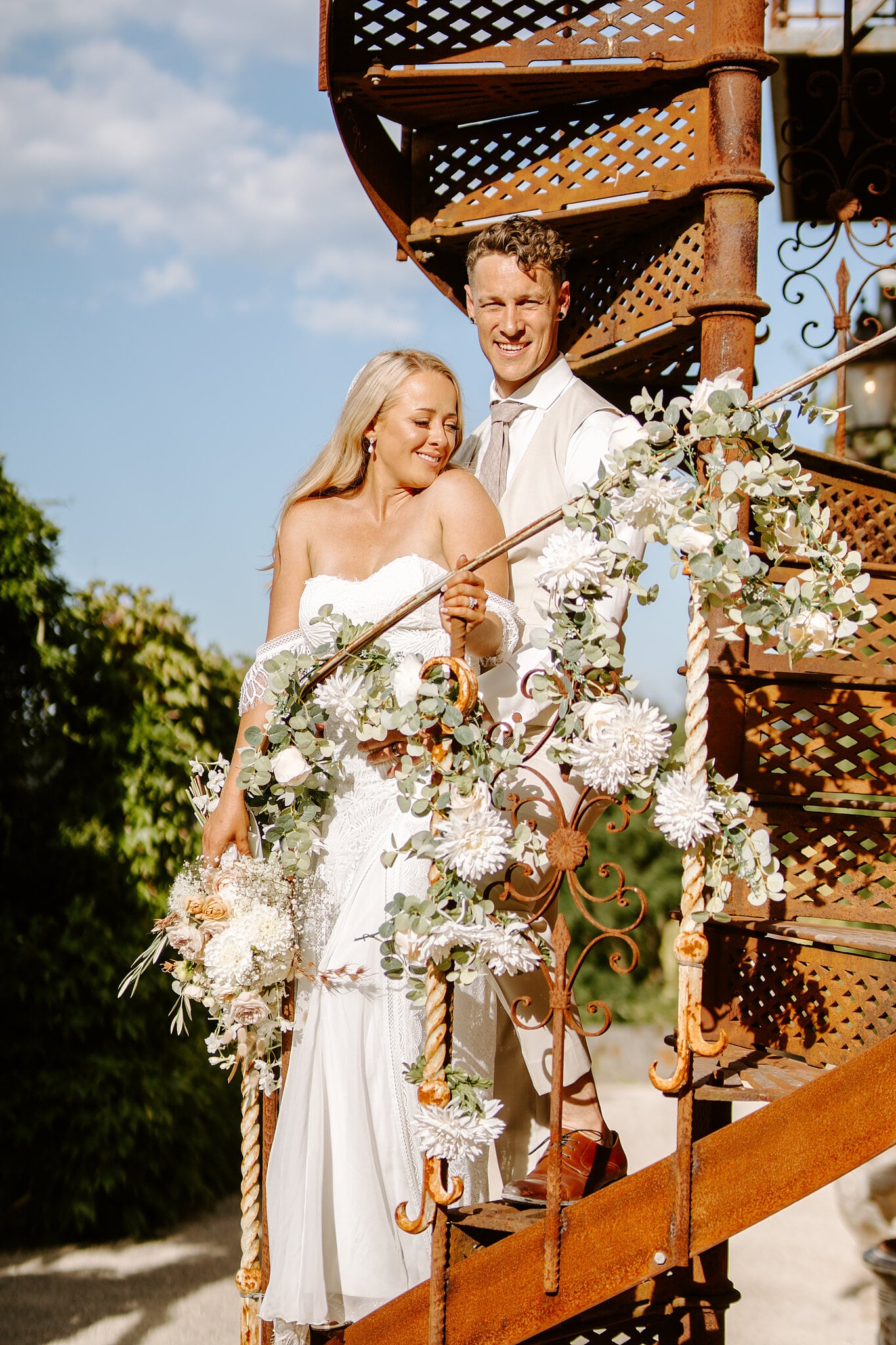 Samantha and Harrison on the flower-wrapped spiral staircase at Mont du Soleil, blue sky behind.