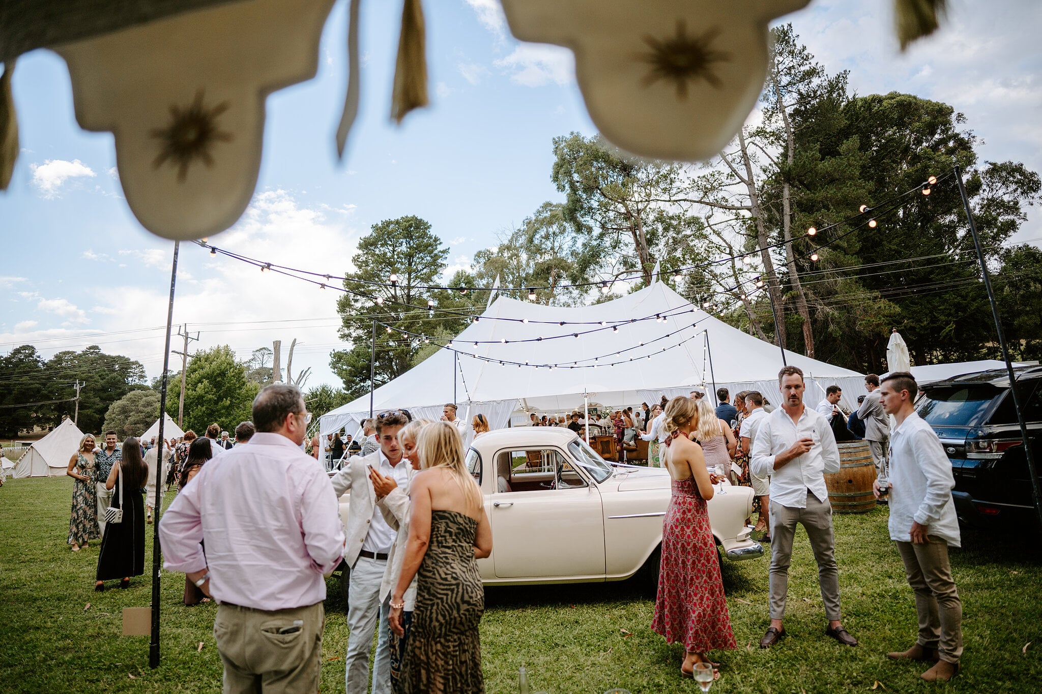 Guests mingle on the lawn around the vintage ute and white marquee under festoon lights.