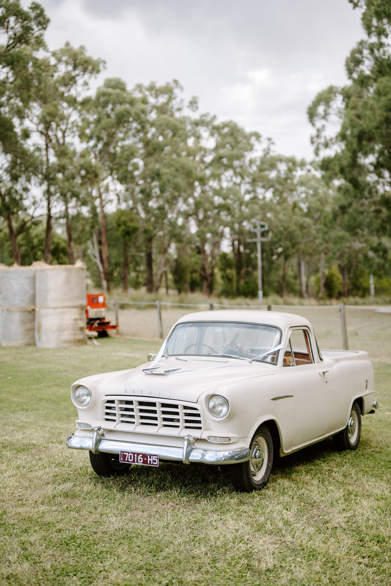 The cream 1959 Holden FC ute parked on the grass beside wrapped hay bales.