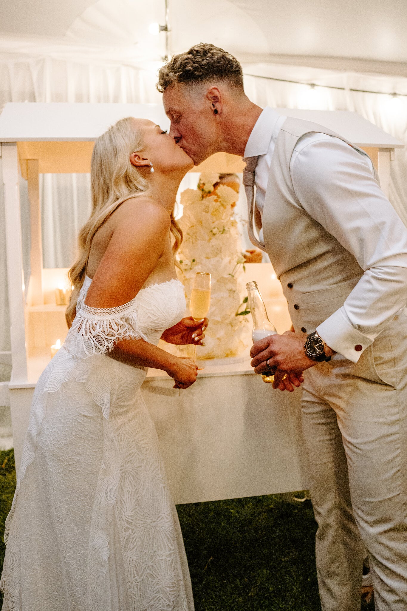 Samantha and Harrison kiss beside the cake, champagne and beer in hand.