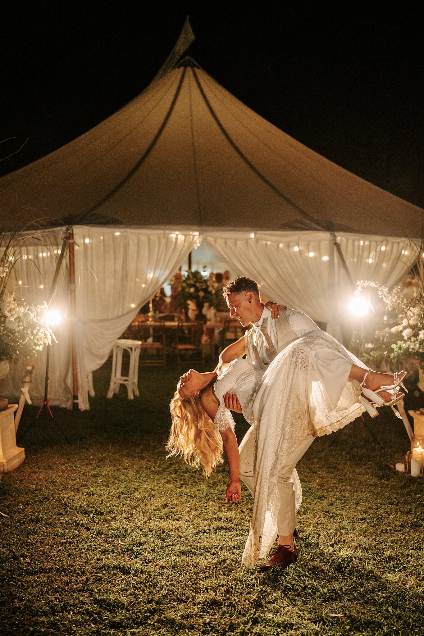 Harrison dips Samantha low on the grass in front of the lit marquee.
