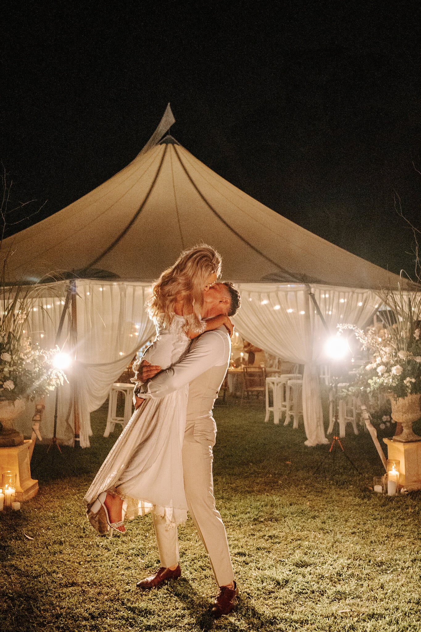 Harrison lifts Samantha for a kiss outside the glowing marquee at night.