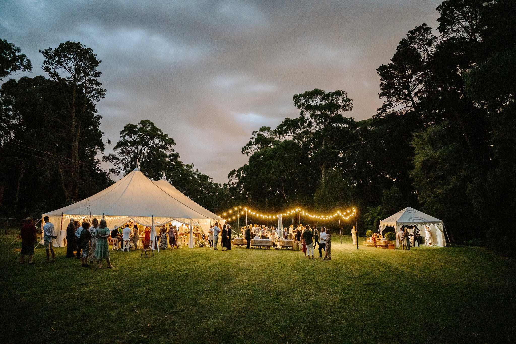 Dusk falls over the marquees, festoon lights and guests on the lawn.