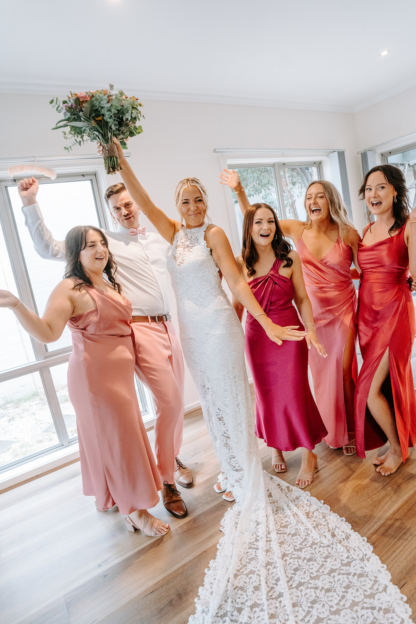 Emma and her bridal party in pink and red satin cheer with their bouquets raised.