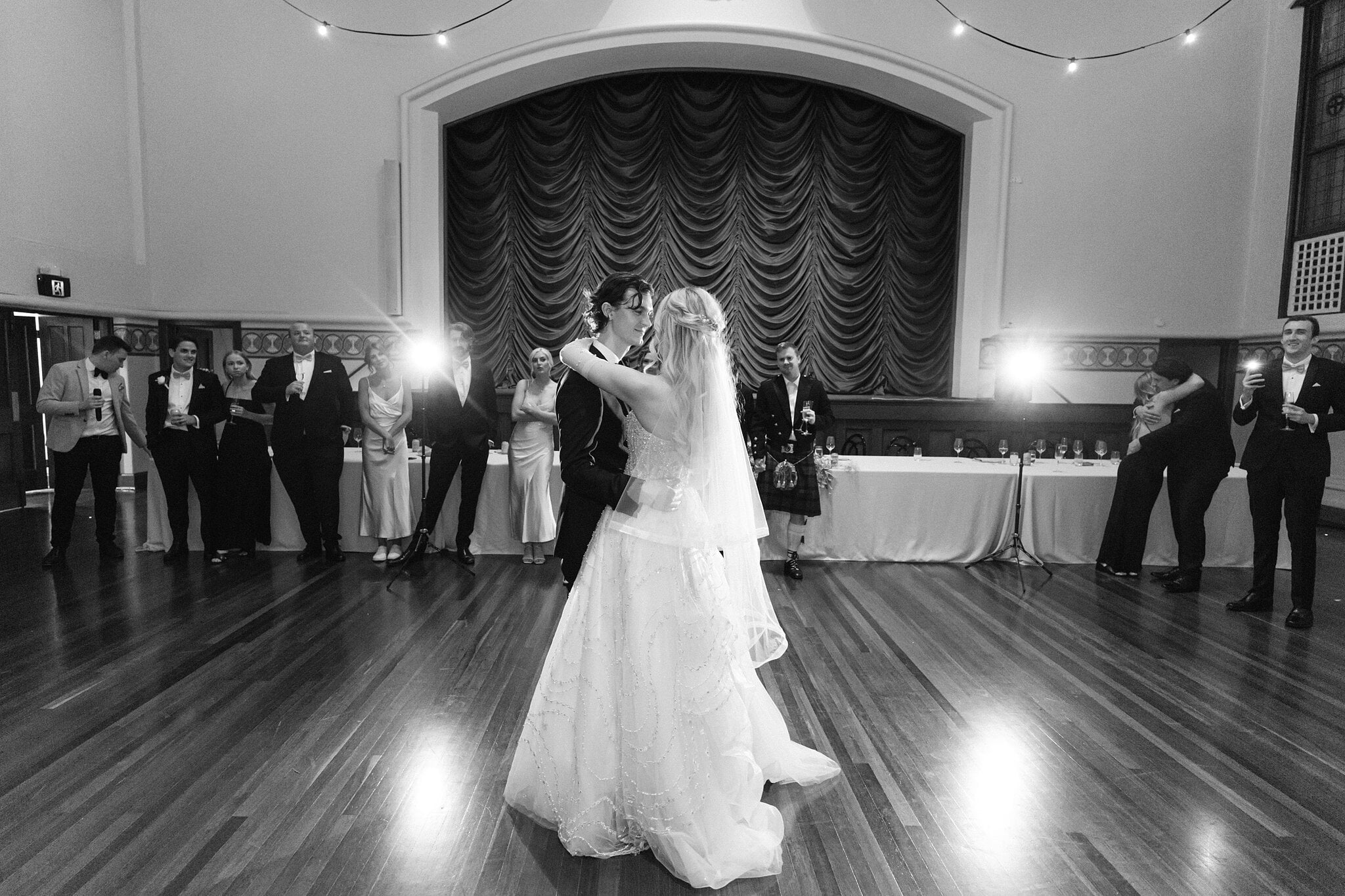 Black and white of Claire and George’s first dance as the bridal party watches from the floor.