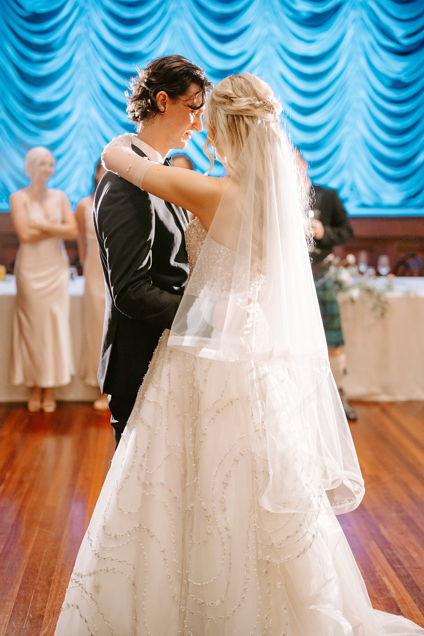 Claire and George rest their foreheads together during their first dance before the blue stage curtain.