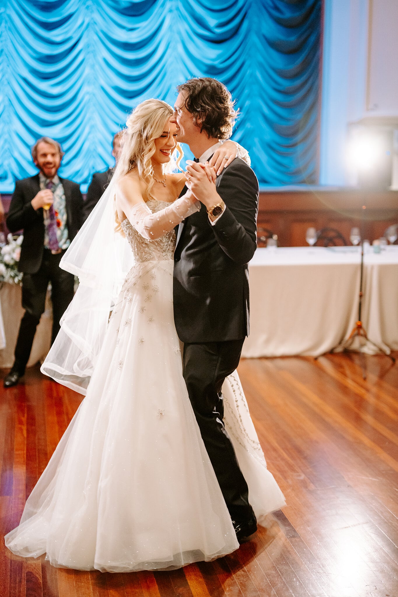 George kisses Claire’s cheek mid dance as a guest raises a glass behind them.