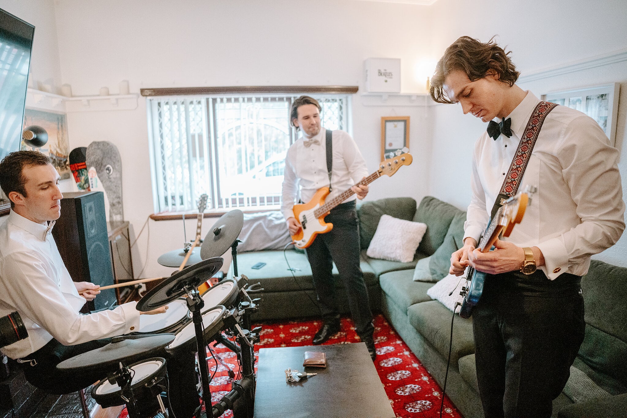 George and two groomsmen jam on drums, bass and guitar in the living room before the wedding.