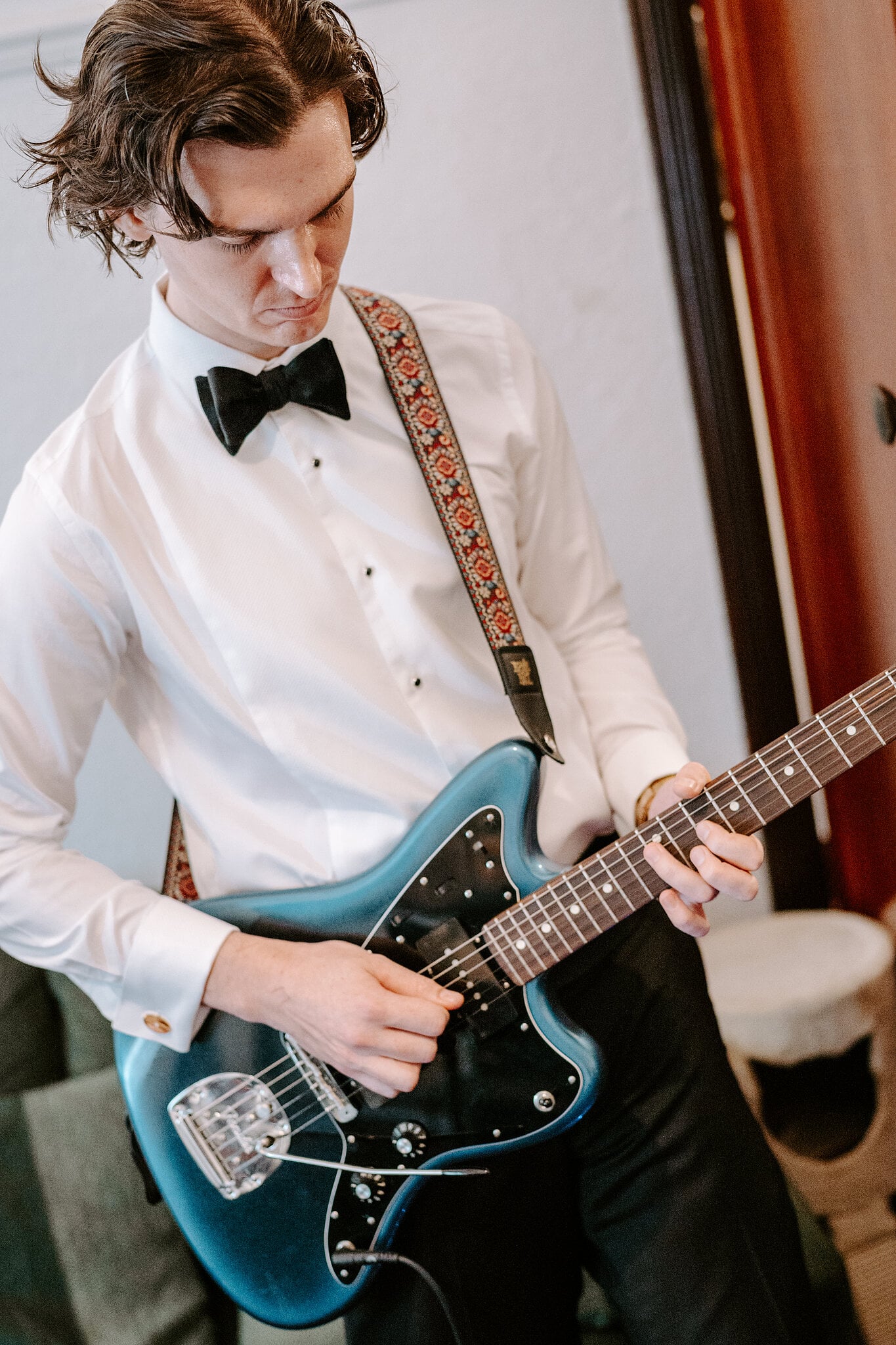 George plays a blue electric guitar in his white shirt and black bow tie.