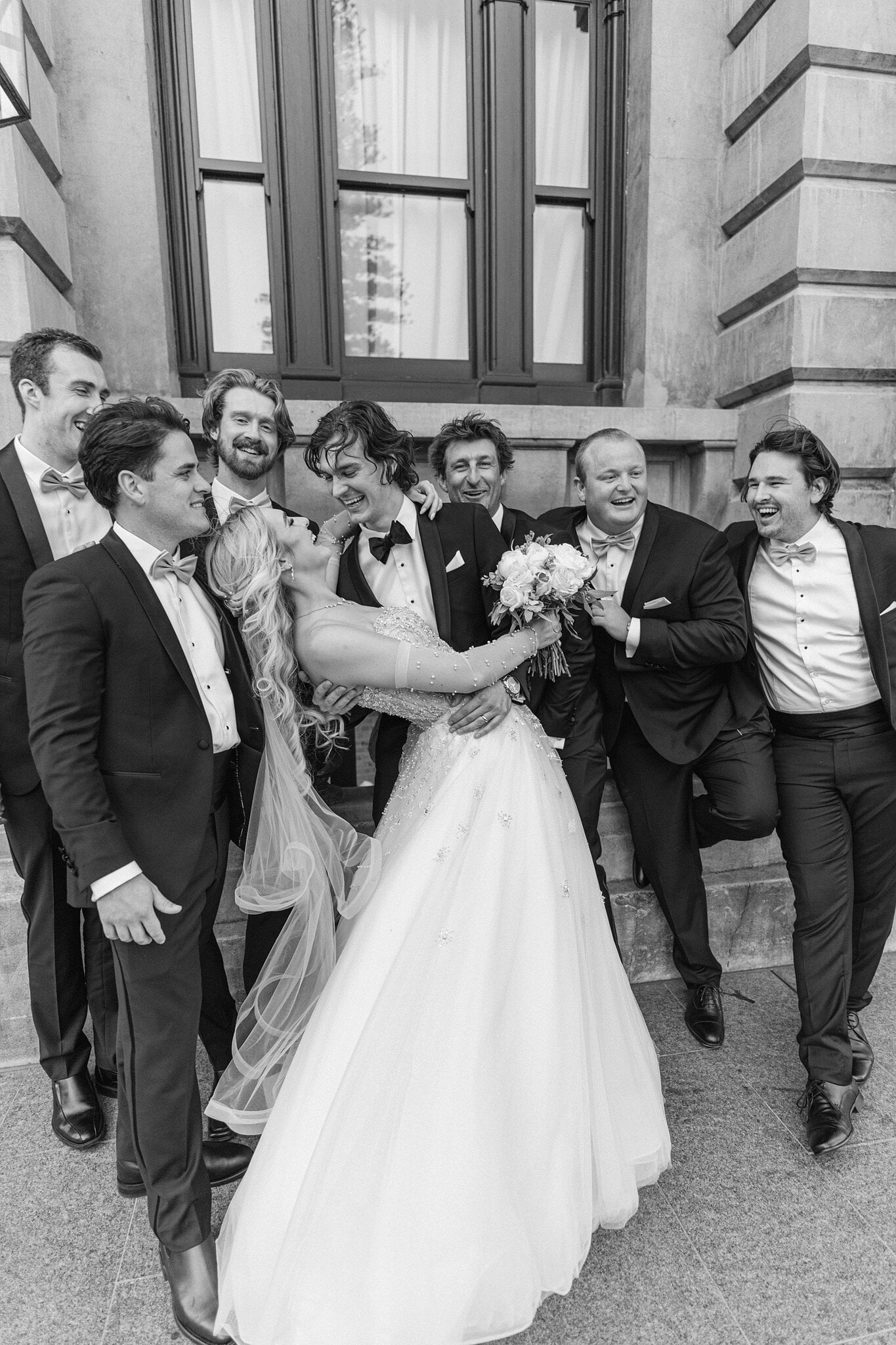 Black and white of George and the groomsmen crowding in around a laughing Claire.