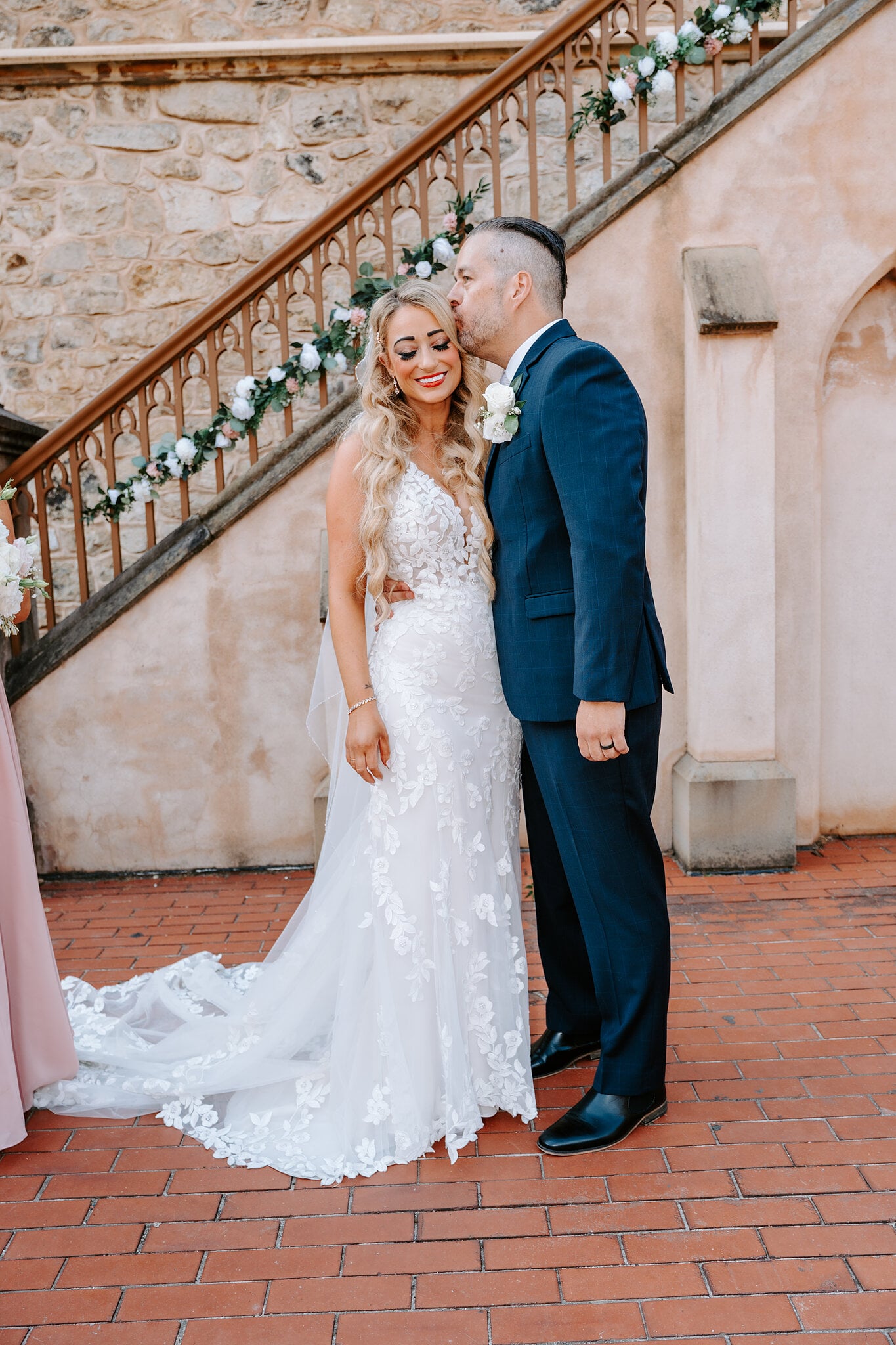 Joe kisses Sarah’s head beside the garlanded stone staircase.