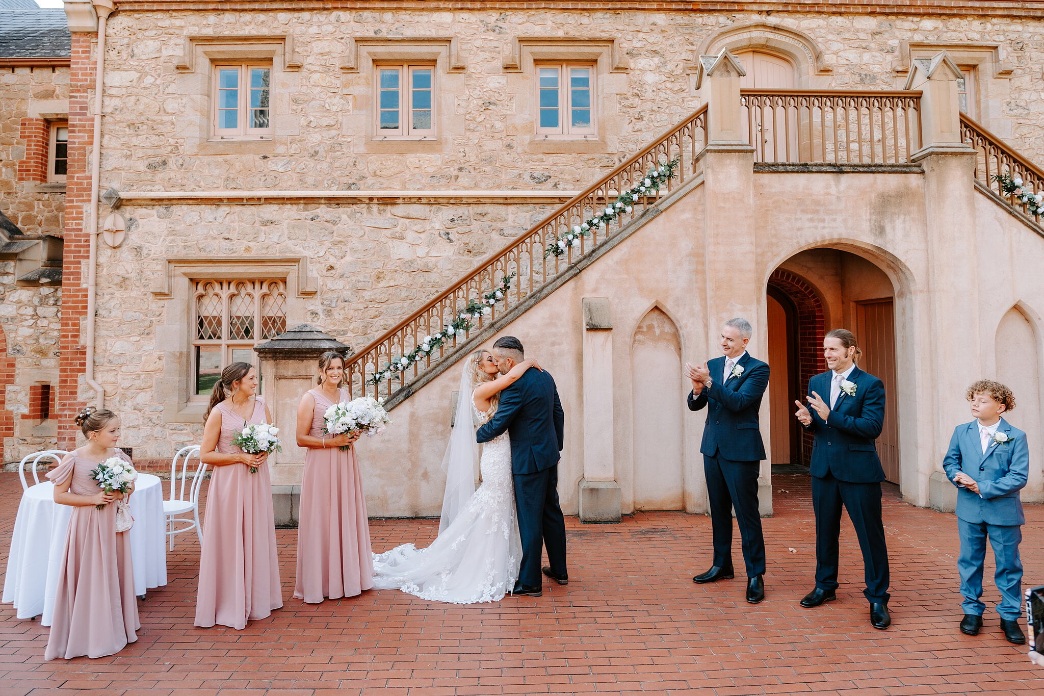 Sarah and Joe kiss as the groomsmen clap beneath the staircase.