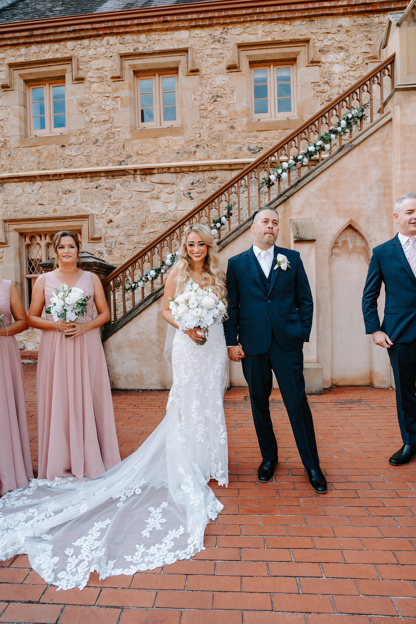 Sarah and Joe stand together as newlyweds beside the garlanded staircase.