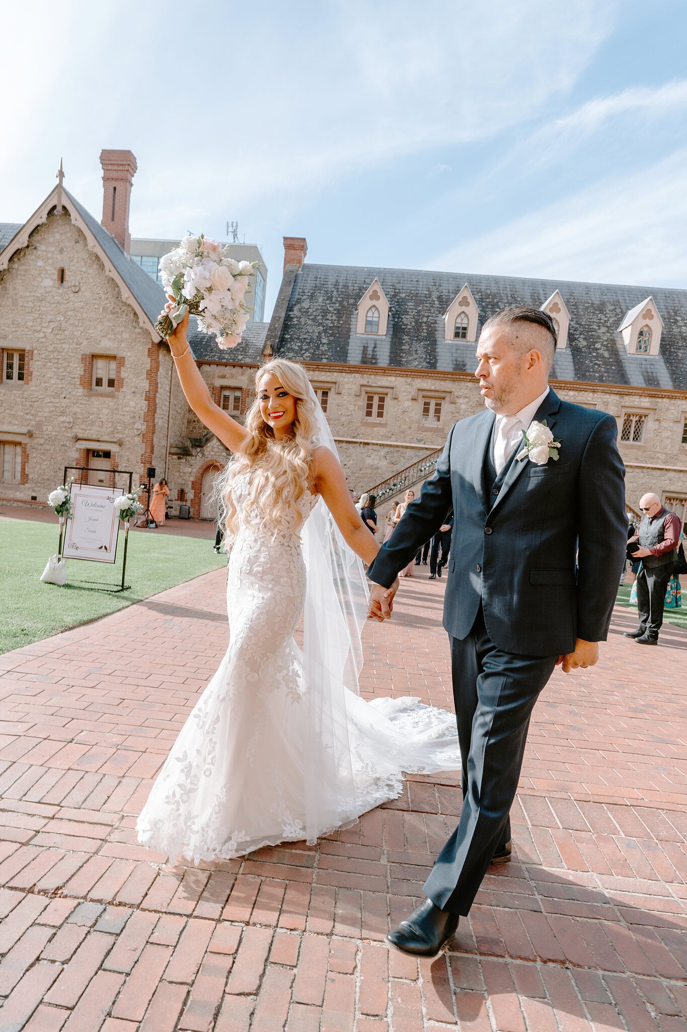 Sarah throws her bouquet in the air as she and Joe walk along the brick path.
