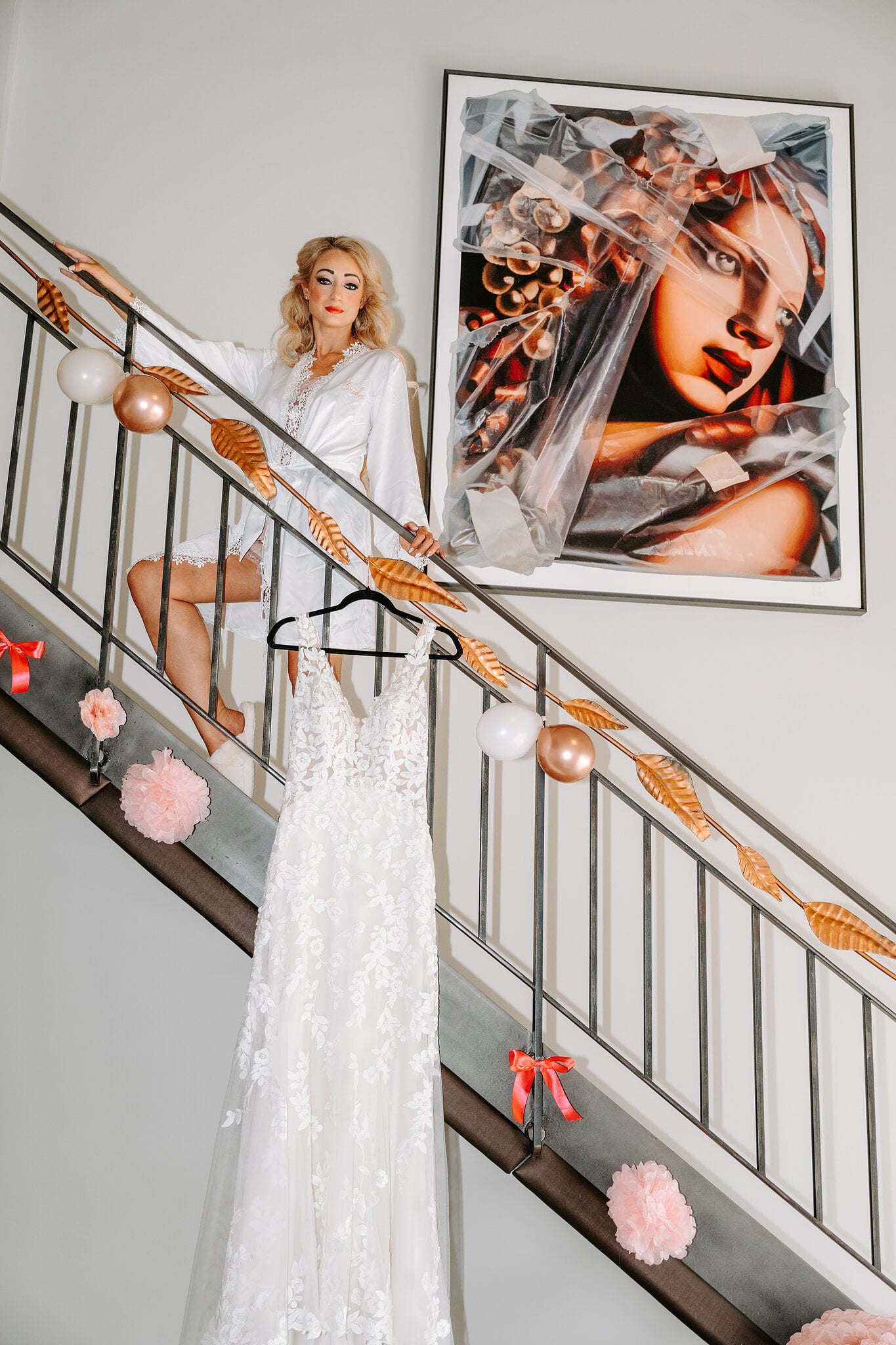 Sarah in a white robe on the suite staircase at The Playford Hotel, her lace gown hanging from the bannister beside a bold portrait painting.