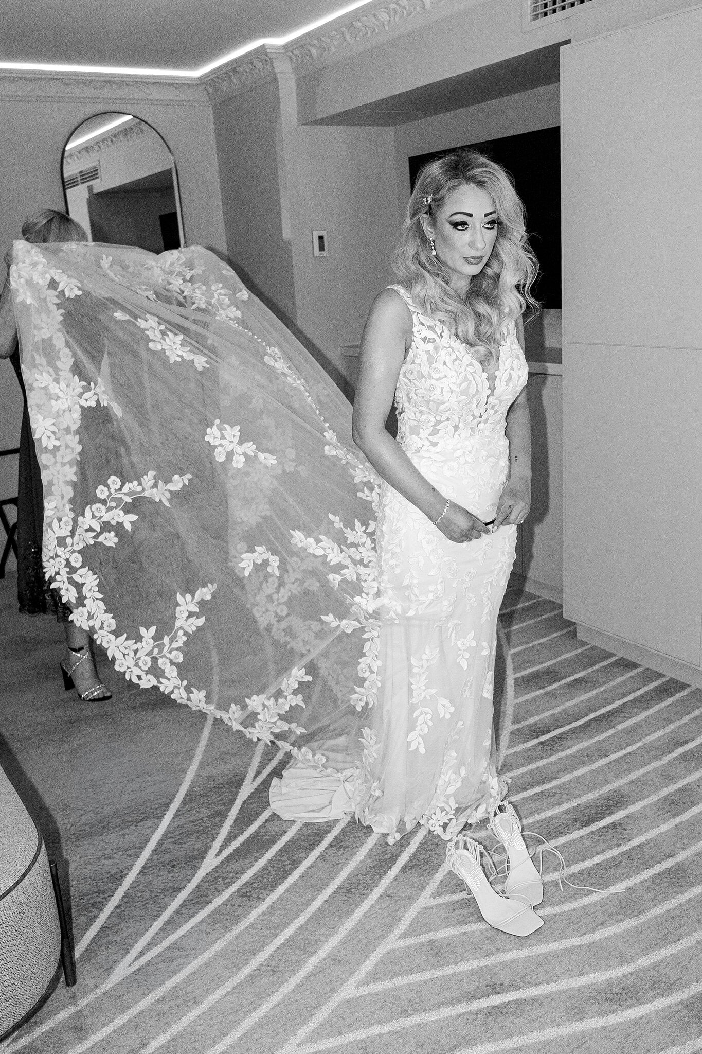 A floral lace veil floats out behind Sarah as it is set in her hair, in black and white.