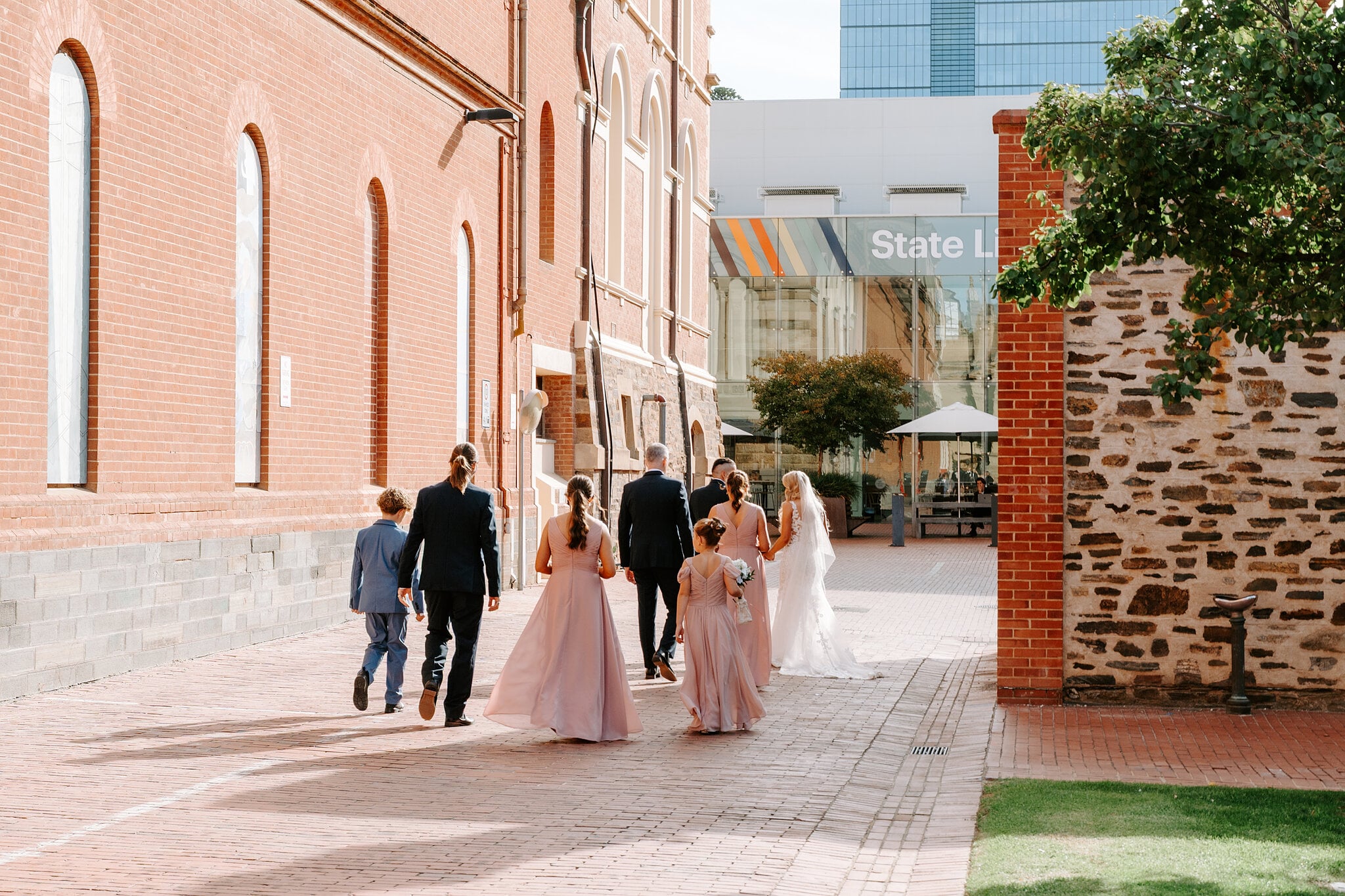 The bridal party walks out between the museum’s red-brick wing and an old stone wall toward North Terrace.