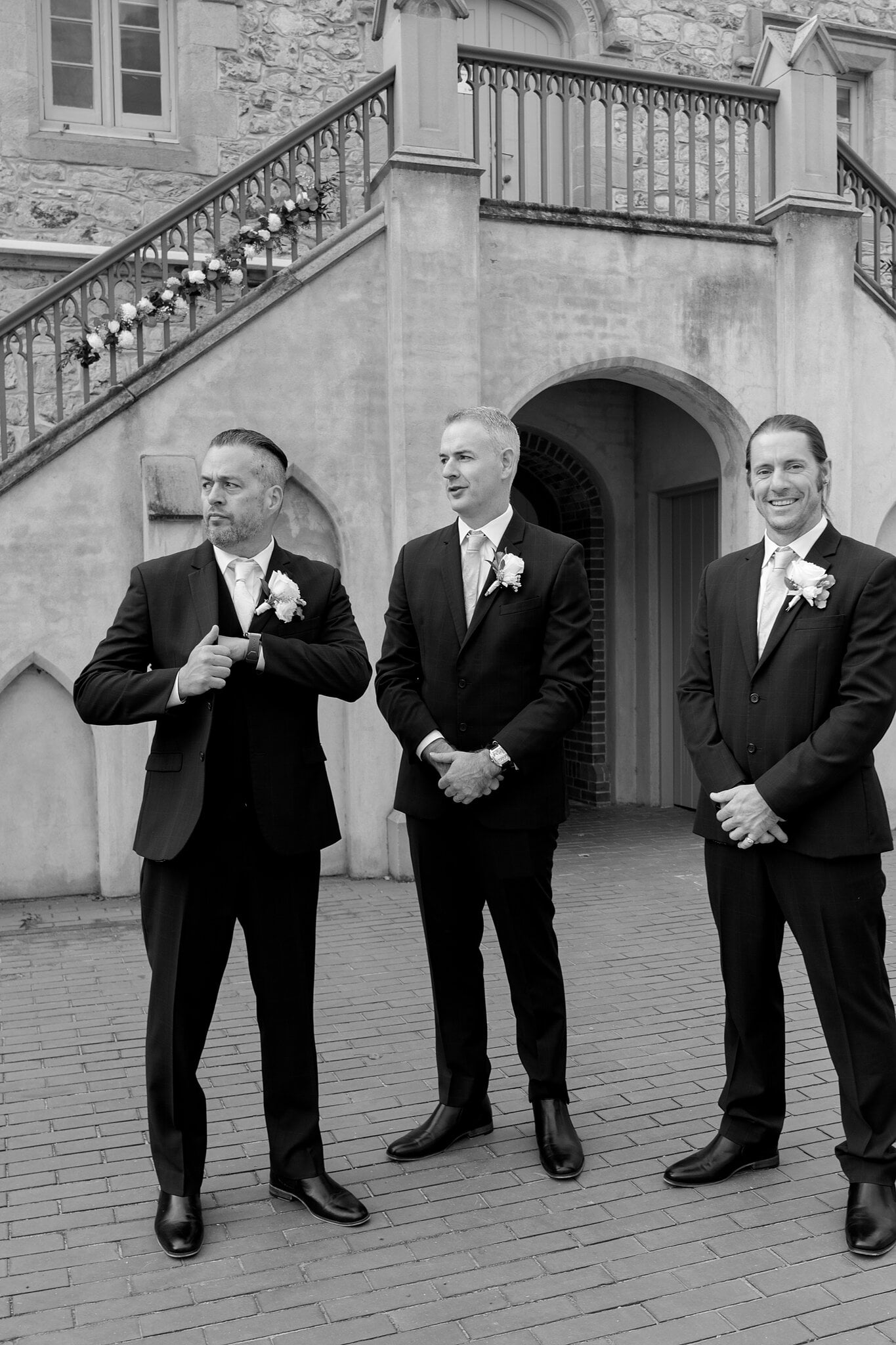 Joe and his groomsmen straighten up under the staircase arch, in black and white.