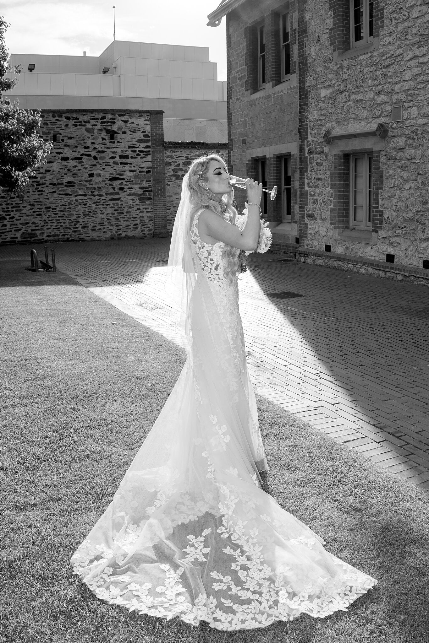 Sarah sips champagne on the courtyard lawn, in black and white.