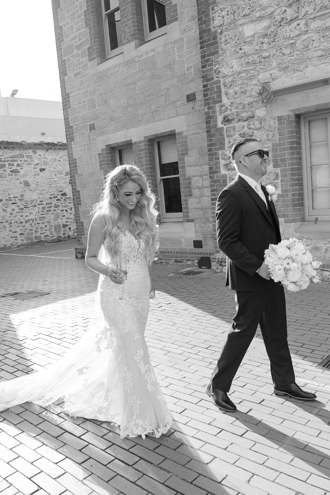 Joe carries Sarah’s bouquet as they stroll across the courtyard, in black and white.