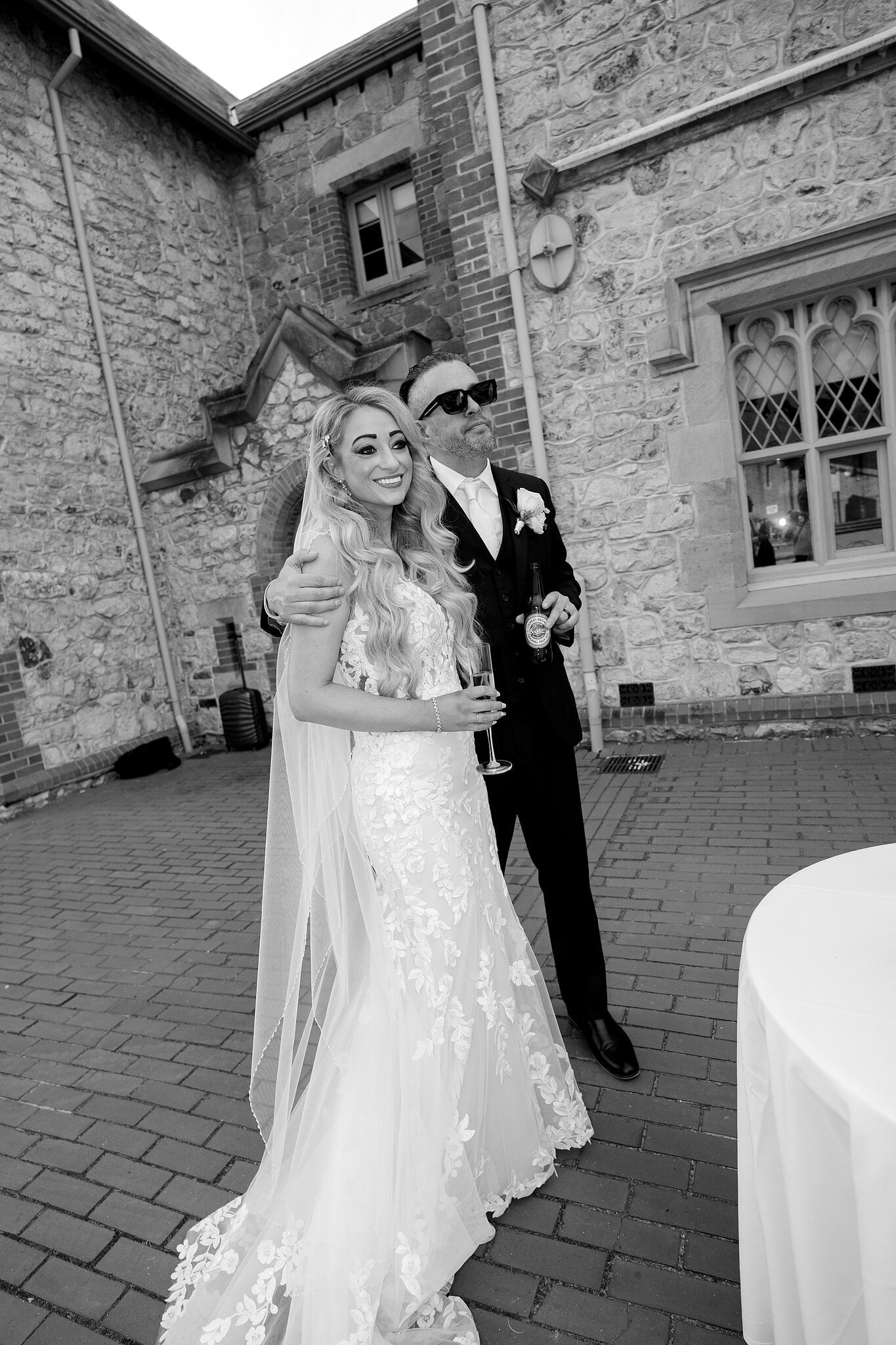 Joe hugs Sarah from behind against the Armoury’s stone walls, in black and white.