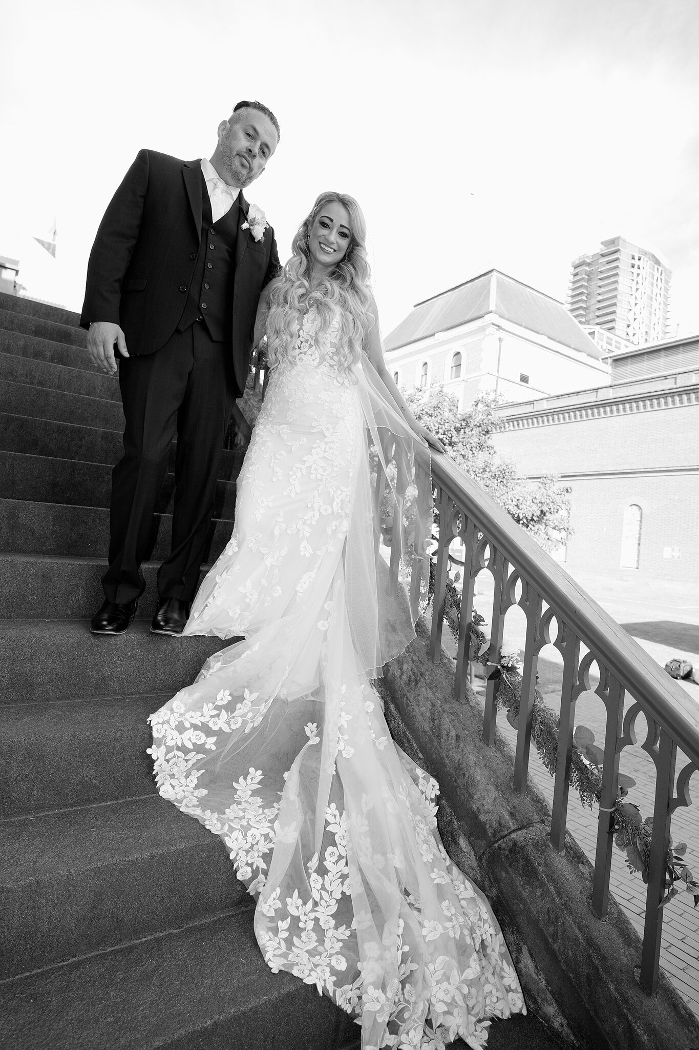 Sarah and Joe stand on the stone staircase, her lace train trailing down the steps, in black and white.