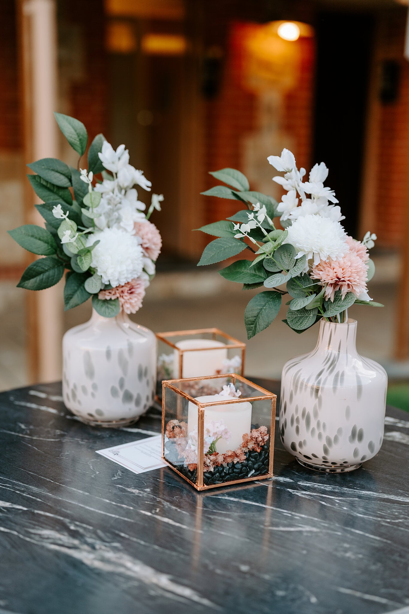 Blush and white flowers in speckled vases beside copper-framed candle boxes.
