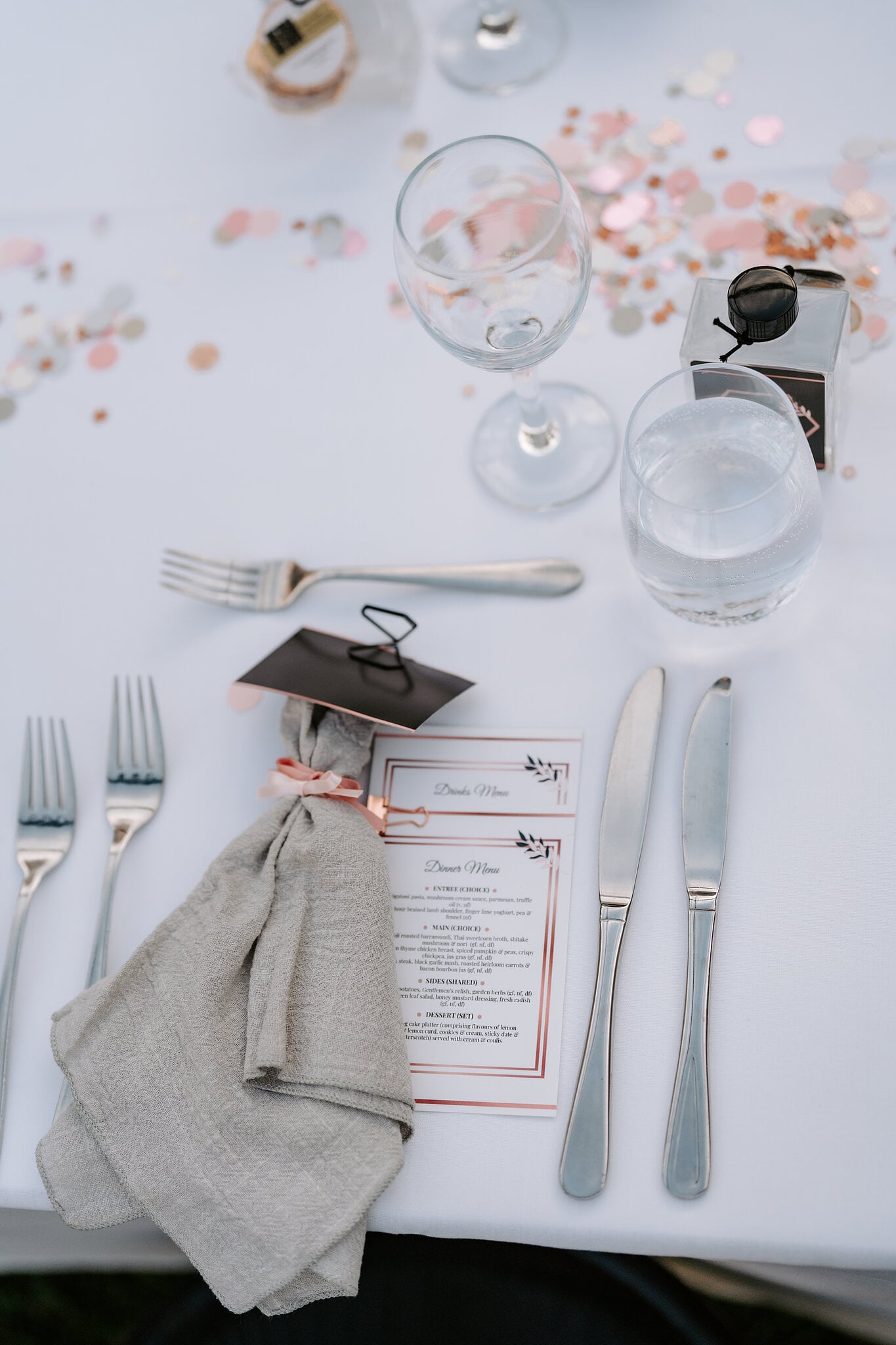 A place setting with a linen napkin, a menu card and rose-gold confetti.