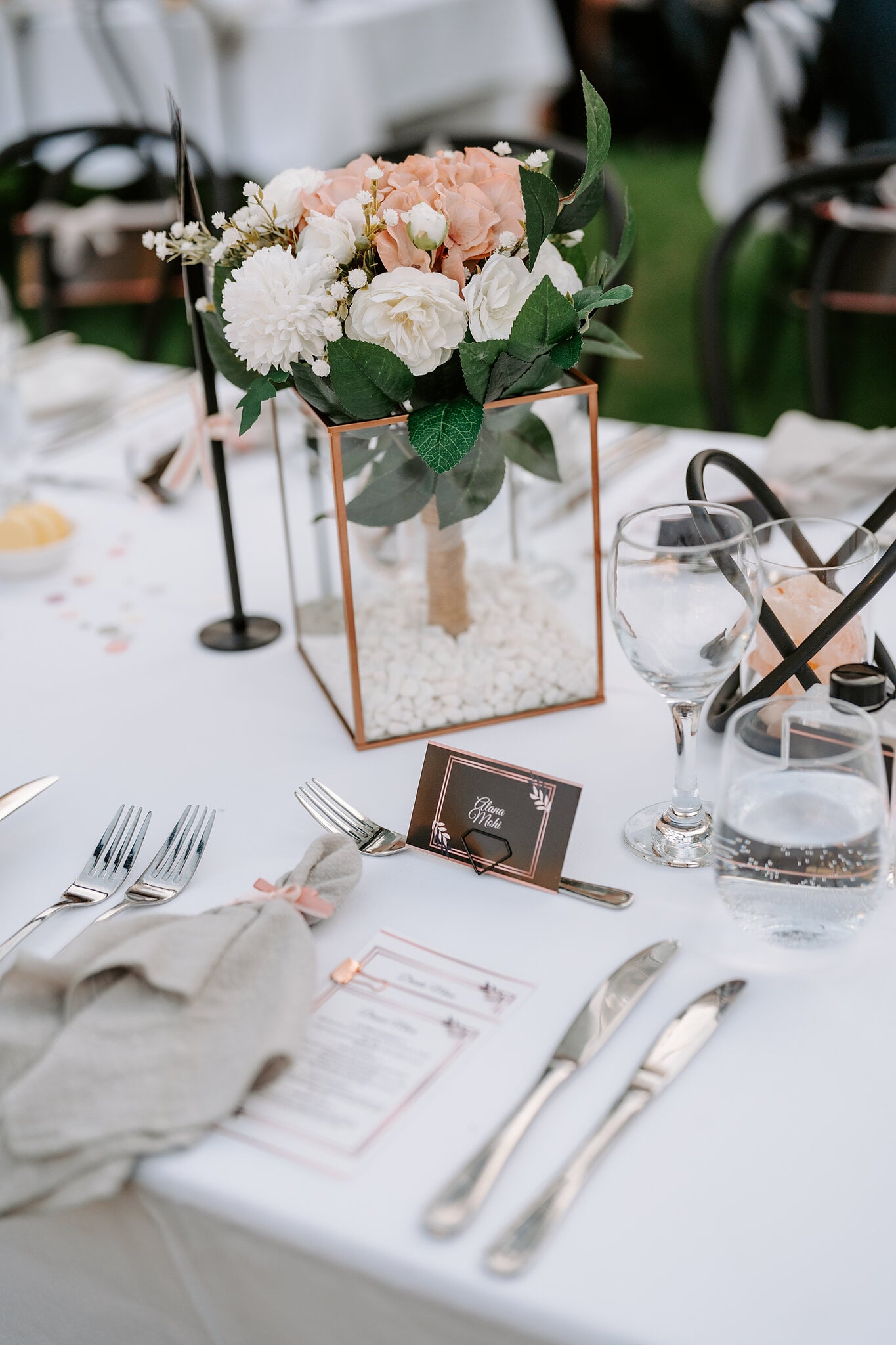 A blush and white centrepiece in a copper-framed glass box above the menu cards.