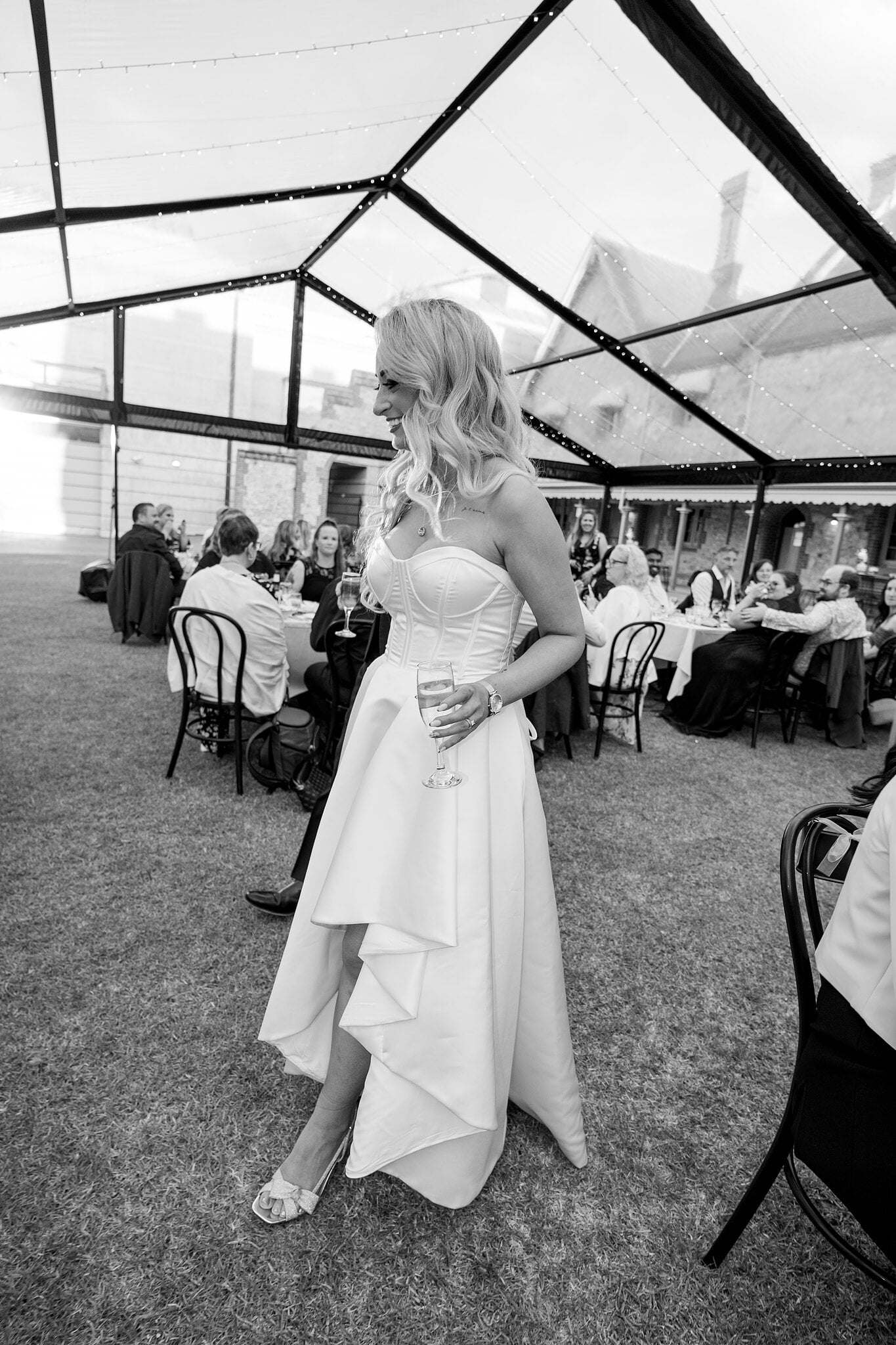 Sarah chats with guests in the marquee, champagne in hand, in black and white.