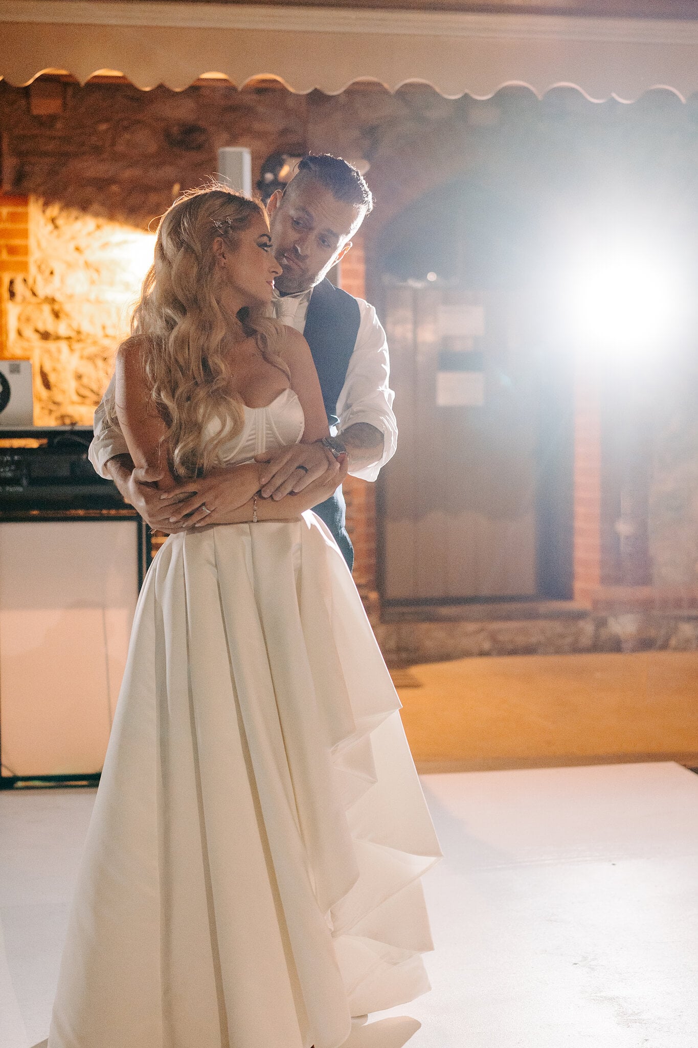 Joe holds Sarah from behind on the dance floor in warm evening light.