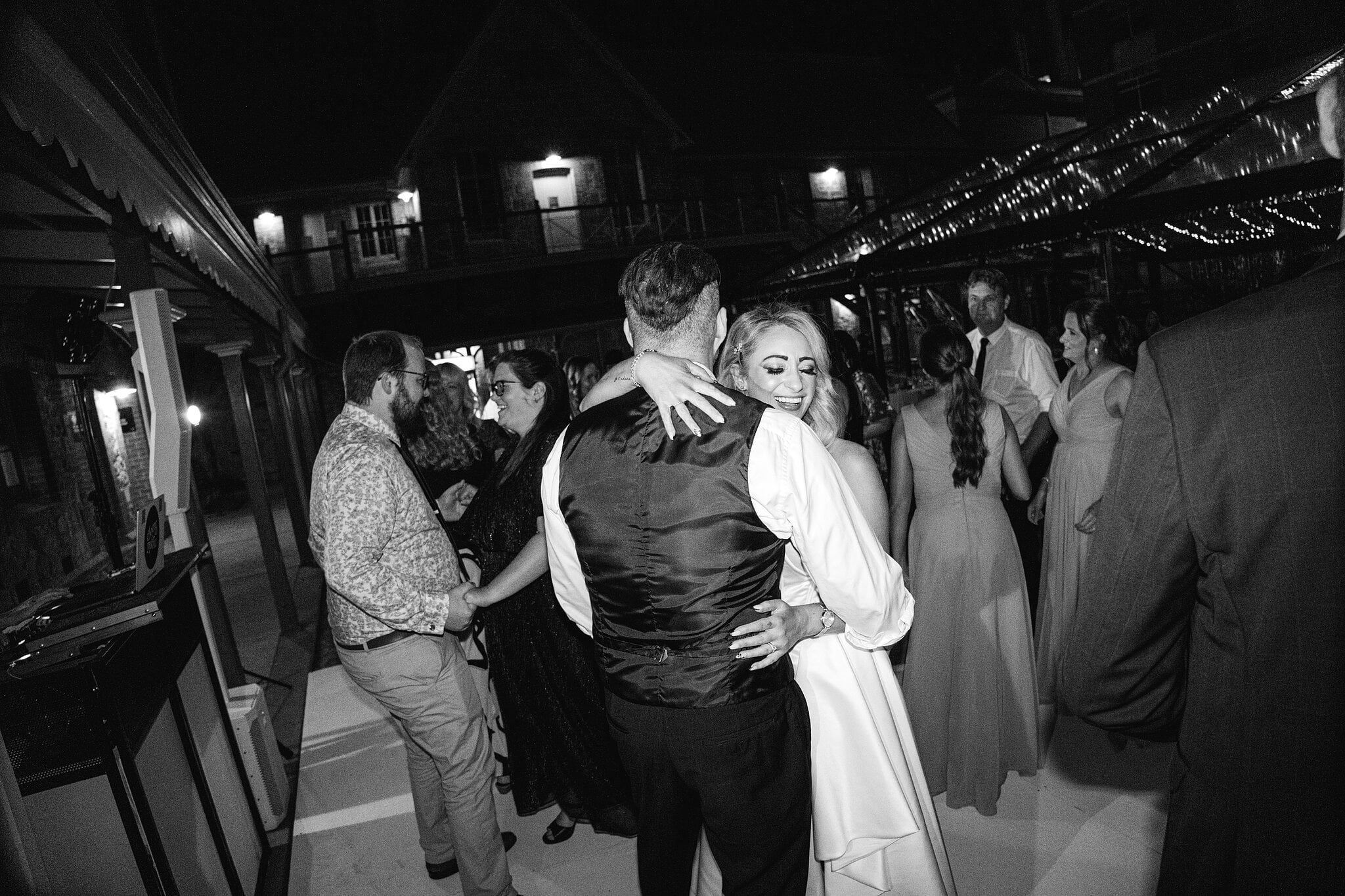 Sarah shares a hug on the crowded dance floor beside the verandah, in black and white.