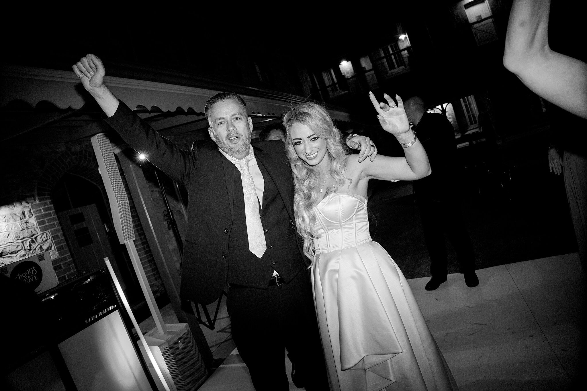 Sarah and Joe throw their arms up on the dance floor, in black and white.