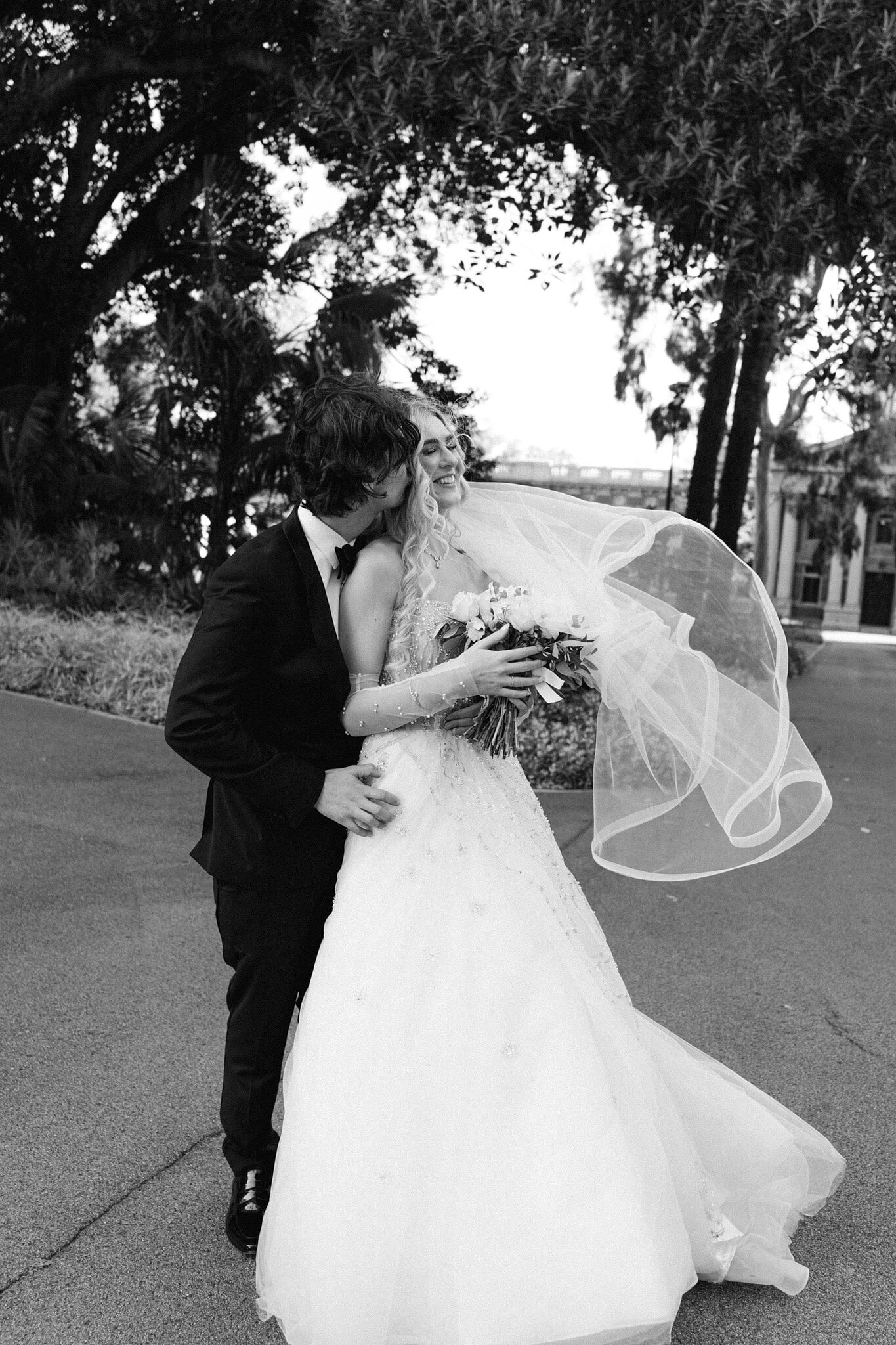 Black and white of George kissing Claire as her veil swirls under the trees.
