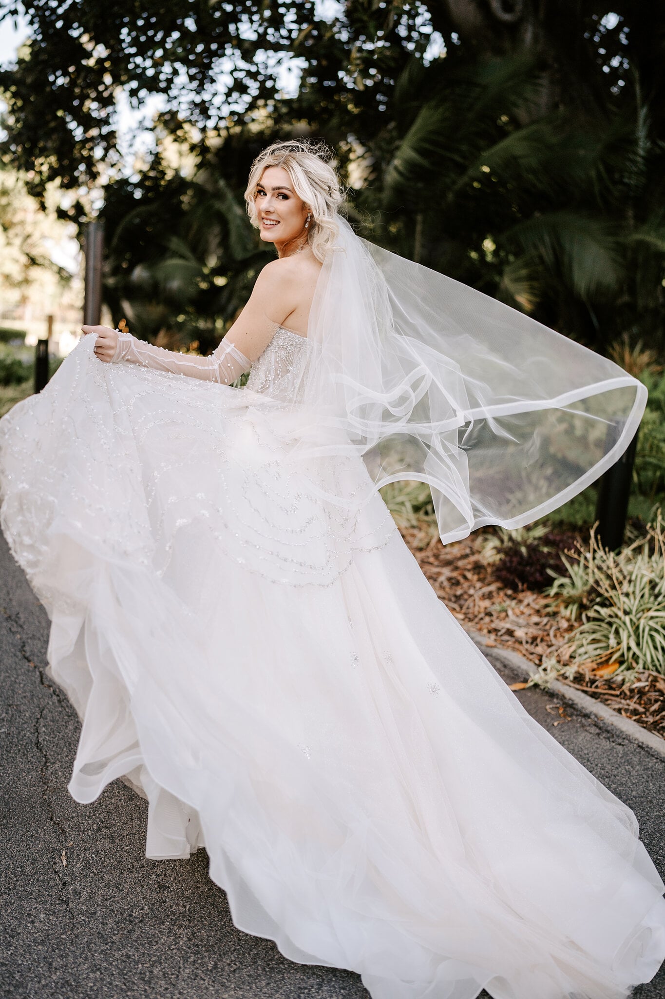 Claire glances back and fans out her ballgown and veil among the palms of the gardens.