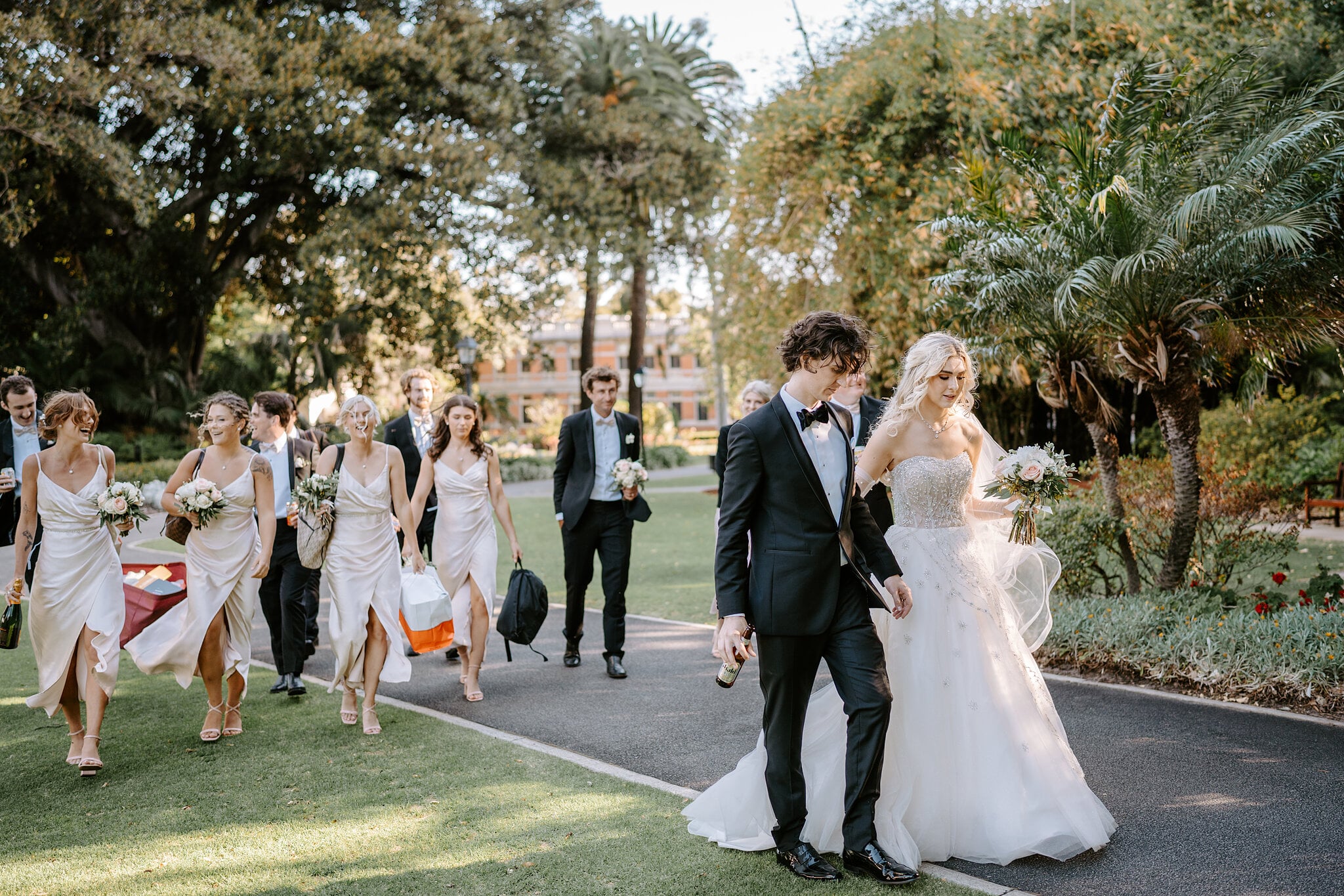 The bridal party strolls through the Supreme Court Gardens, palms overhead and champagne in hand.