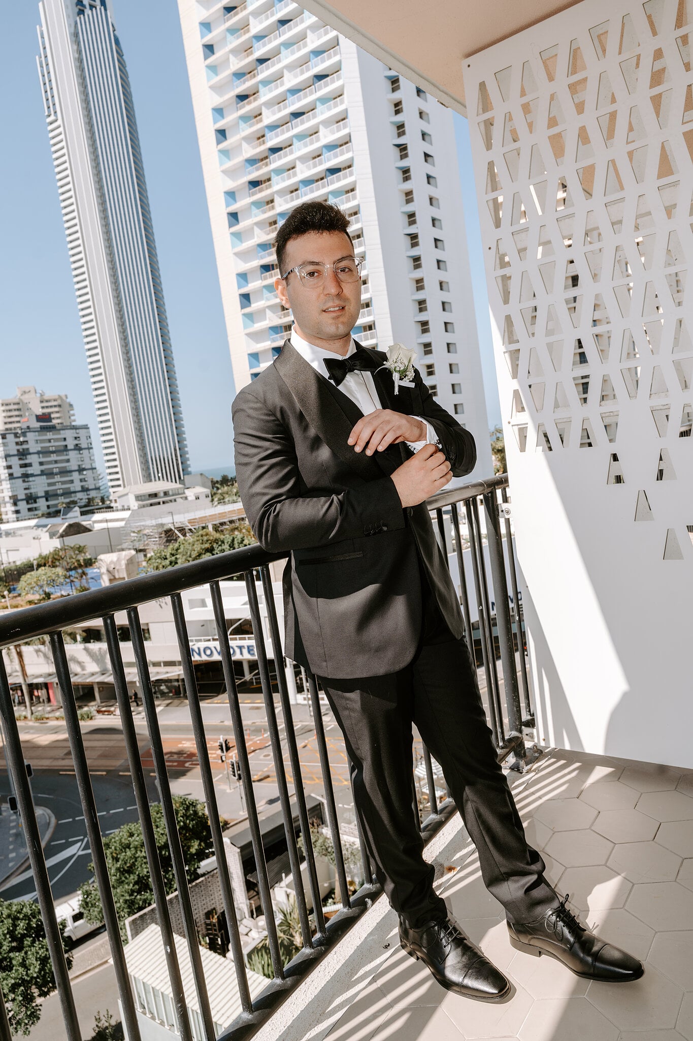 Jordan fixes his cuffs on his balcony at The Island, Surfers Paradise towers rising behind him.