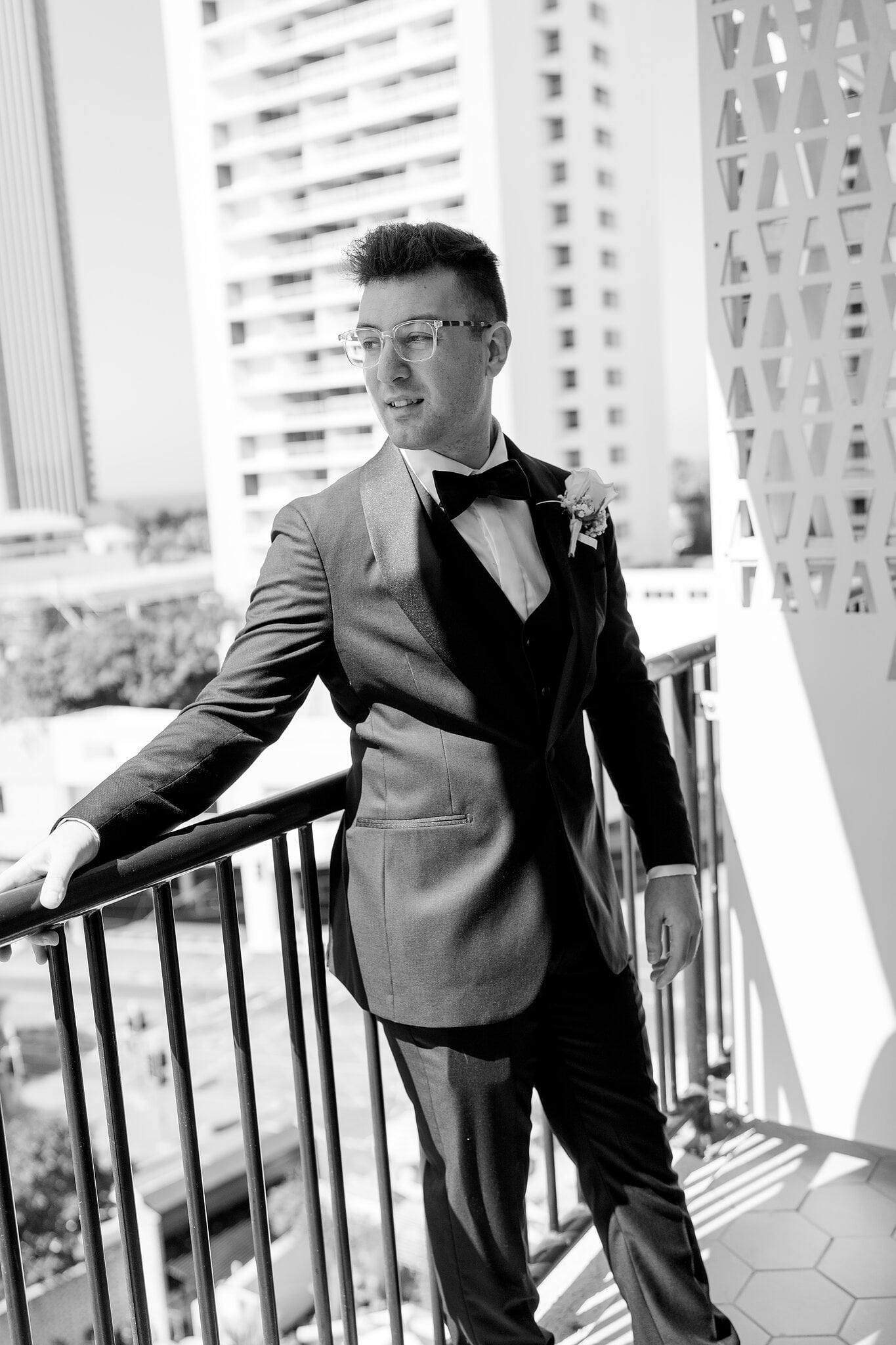 Jordan leans on the balcony rail in his tuxedo and looks out over Surfers Paradise, in black and white.