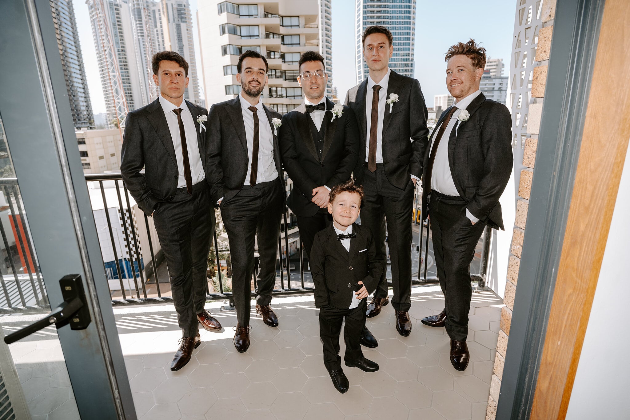 Jordan, his groomsmen and the littlest groomsman line up on a balcony above Surfers Paradise.