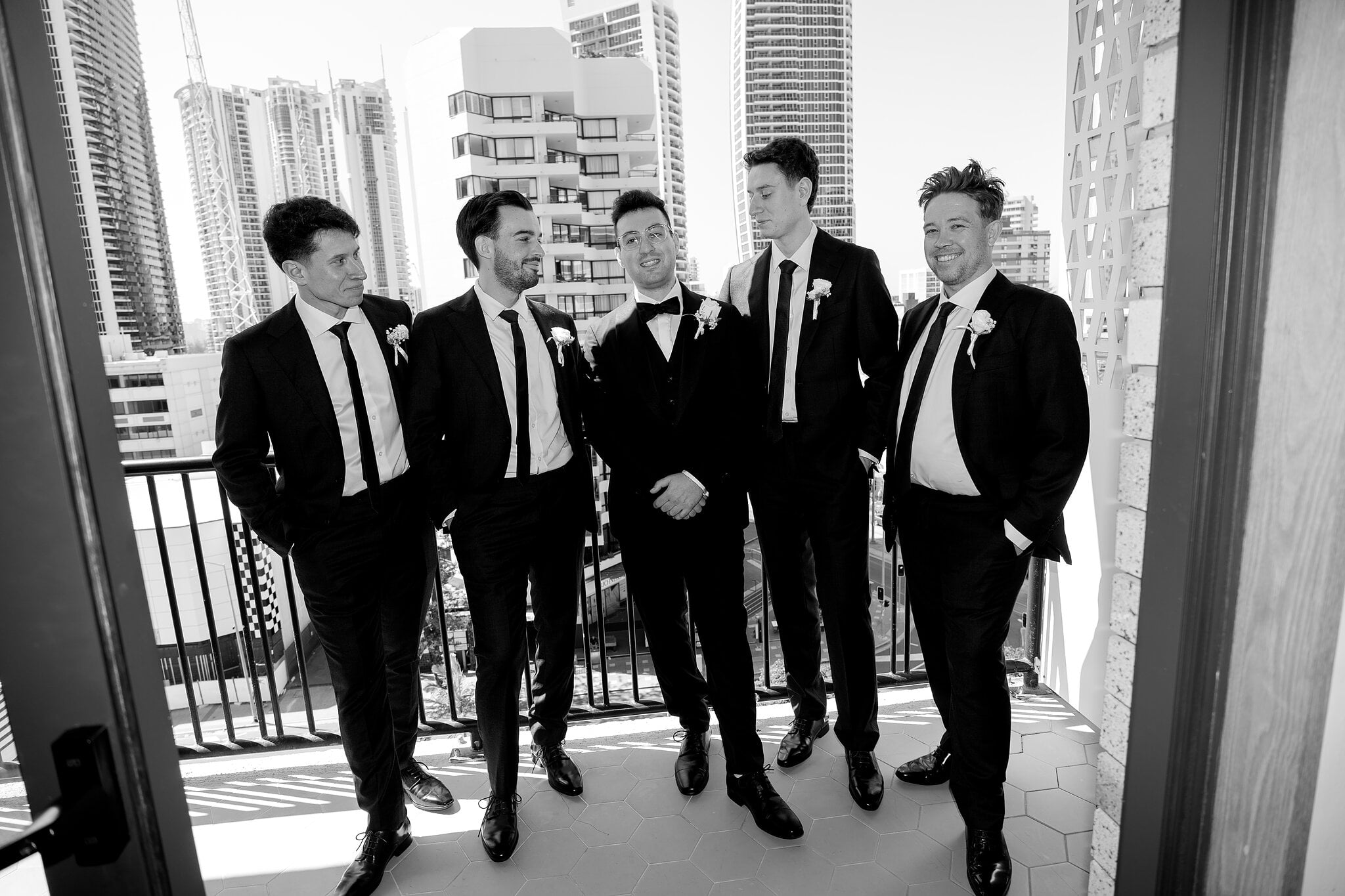 Jordan and his groomsmen share a laugh on the balcony, in black and white.