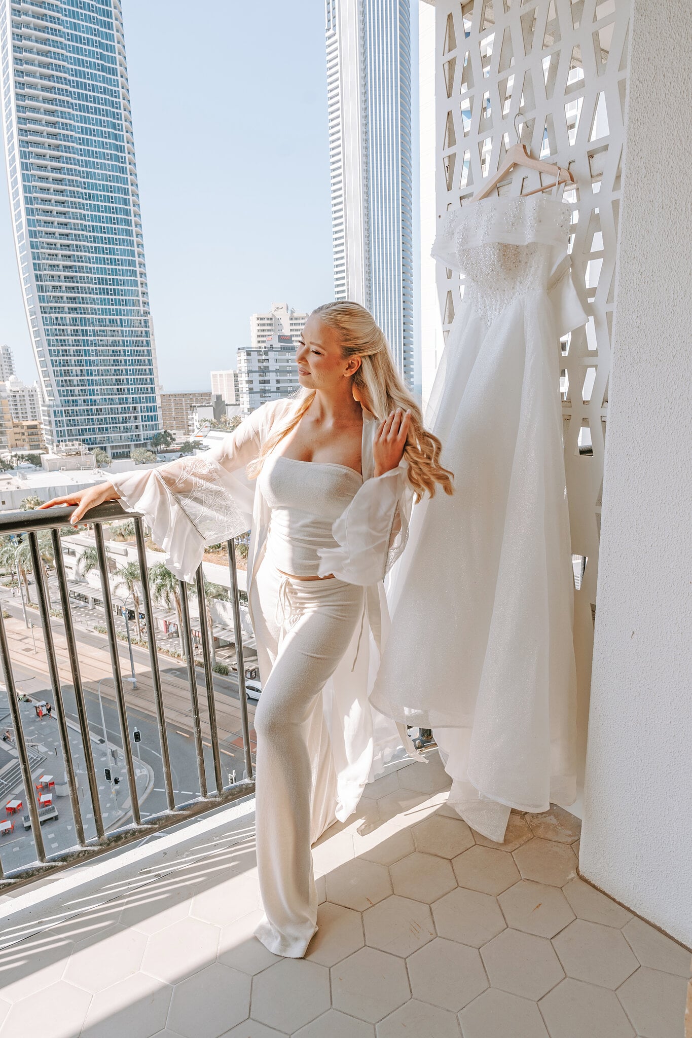 Sorayaa leans on her balcony in a white getting-ready set, her gown hanging beside her above Surfers Paradise Boulevard.