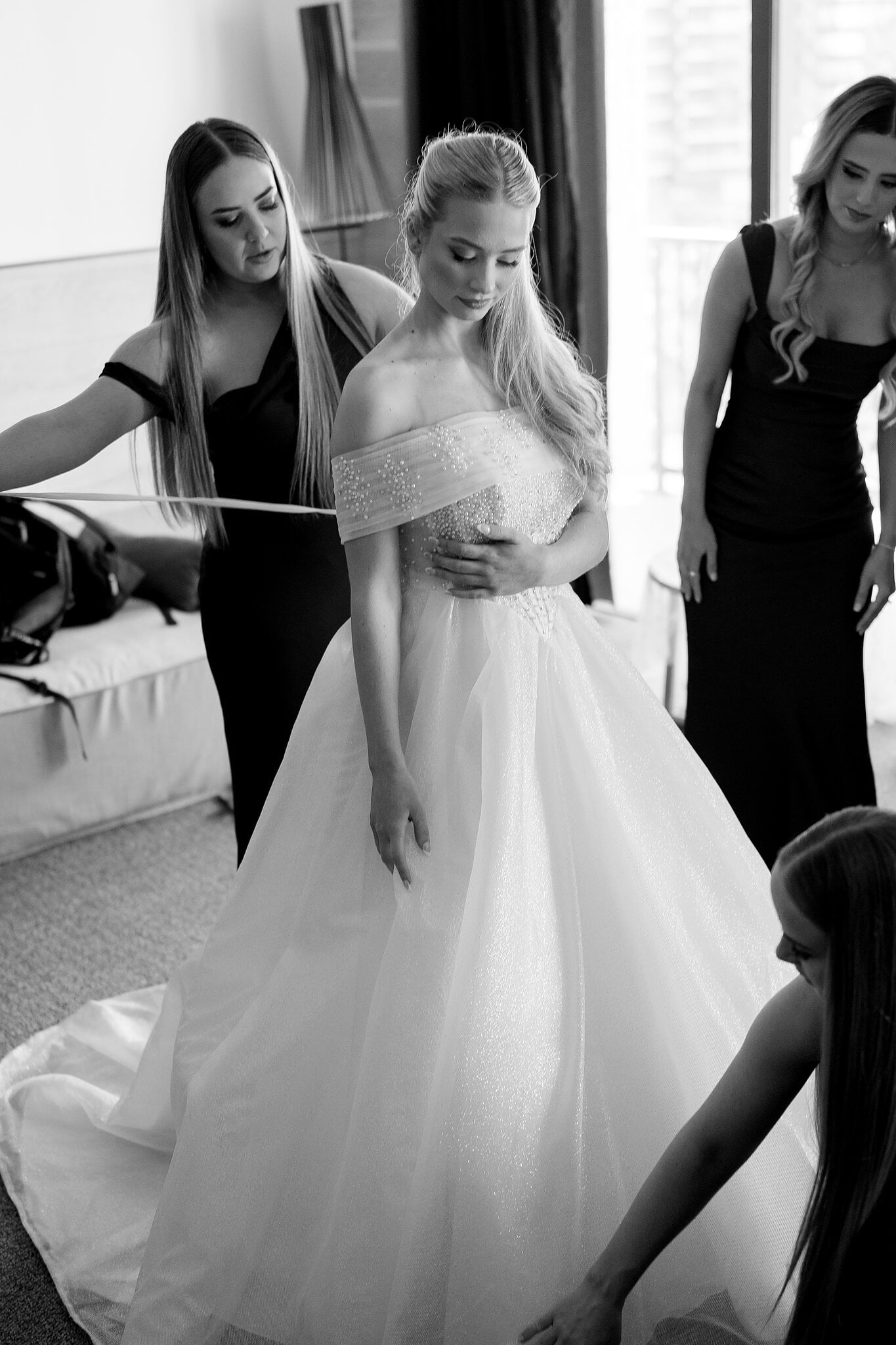 Her bridesmaids lace Sorayaa into her off-the-shoulder ball gown, in black and white.