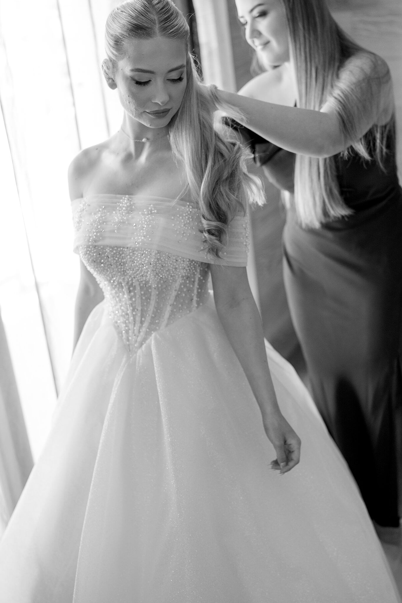 A bridesmaid smooths Sorayaa’s hair over the beaded corset of her gown, in black and white.