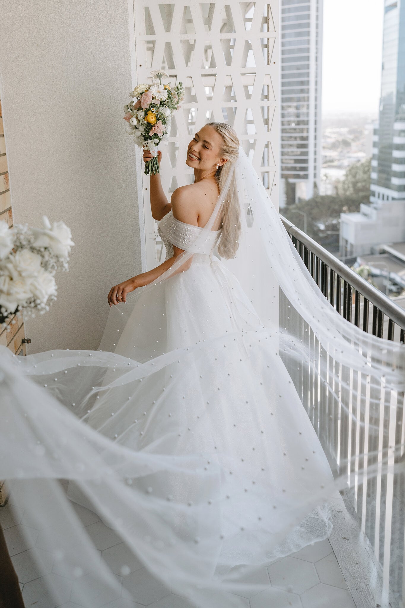 Sorayaa sends her pearl veil flying on the balcony, bouquet held high.