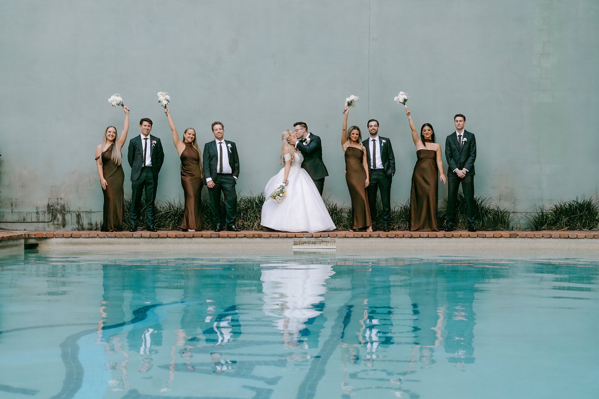 The bridal party raises their bouquets beside the pool at The Island, every figure mirrored in the water.