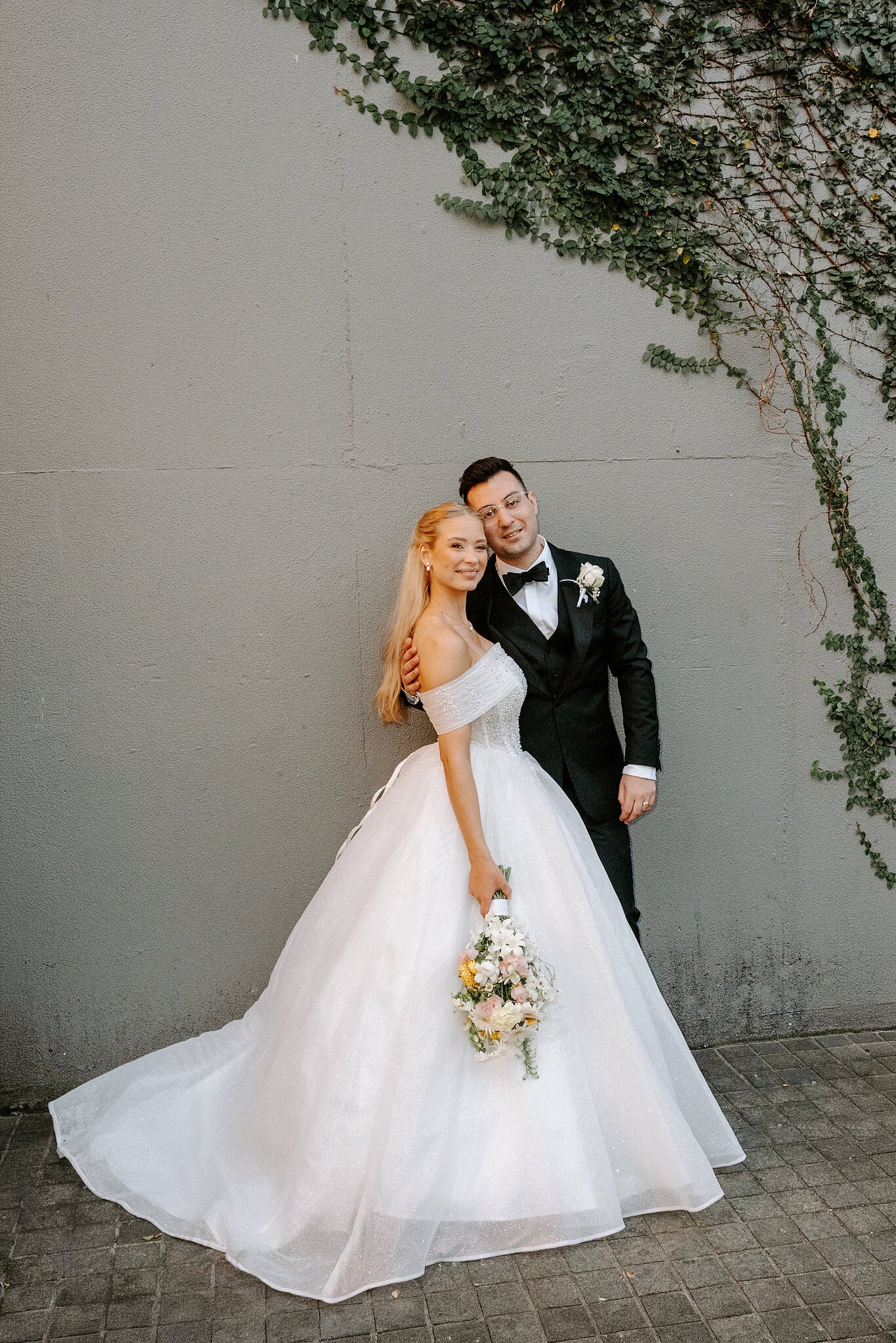 Sorayaa and Jordan cuddle up against the ivy wall, her train fanned across the pavers.