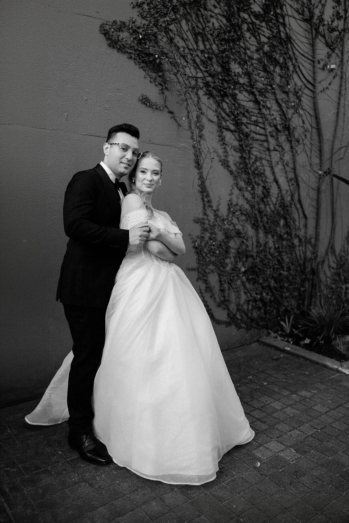 Jordan holds Sorayaa from behind beside the ivy, in black and white.
