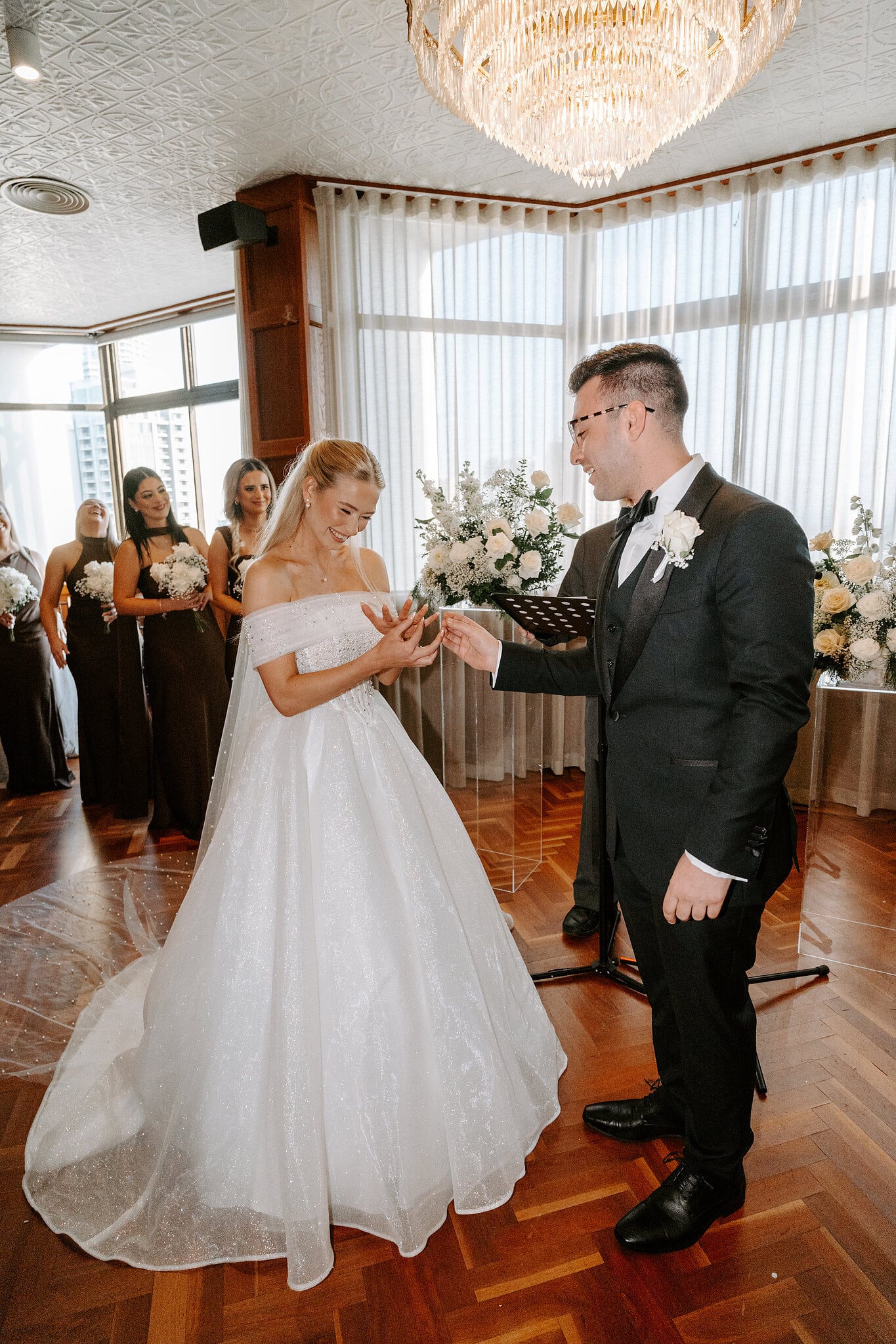 Jordan slides on Sorayaa’s ring beneath the chandelier on the herringbone parquet.