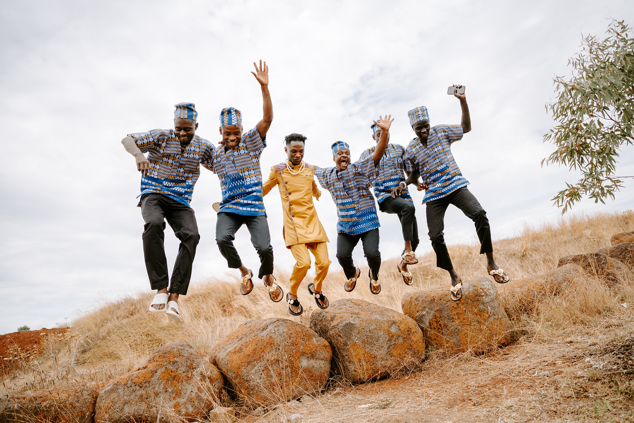 Allen and his groomsmen in matching blue prints and caps leap off a row of boulders.